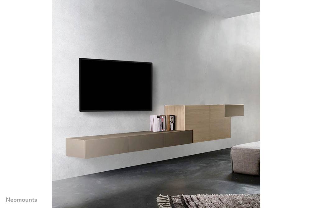Televisore montato su una parete grigia, accanto a uno scaffale elegante con libri. Tappeto su un pavimento scuro, ambiente di un soggiorno moderno.