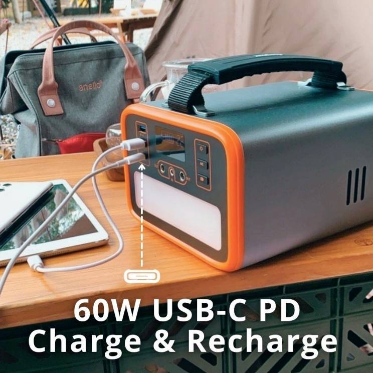Un caricabatterie portatile con la scritta '60W USB-C PD Charge & Recharge' sta caricando un tablet e uno smartphone su un tavolo di legno.