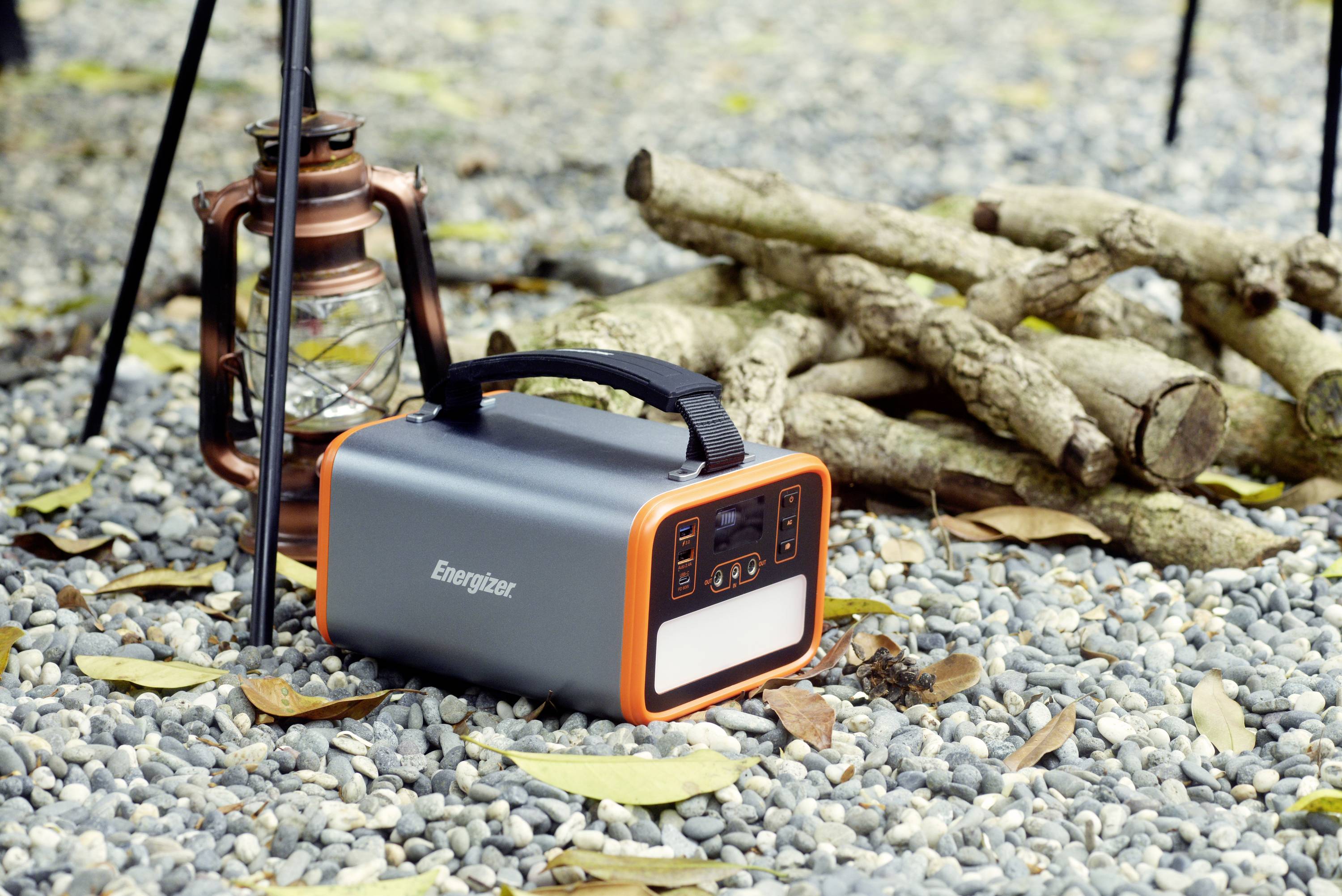 Unità batteria portatile e lanterna su terreno ghiaioso accanto a legna impilata. Scena all'aperto per campeggio o alimentazione di emergenza.
