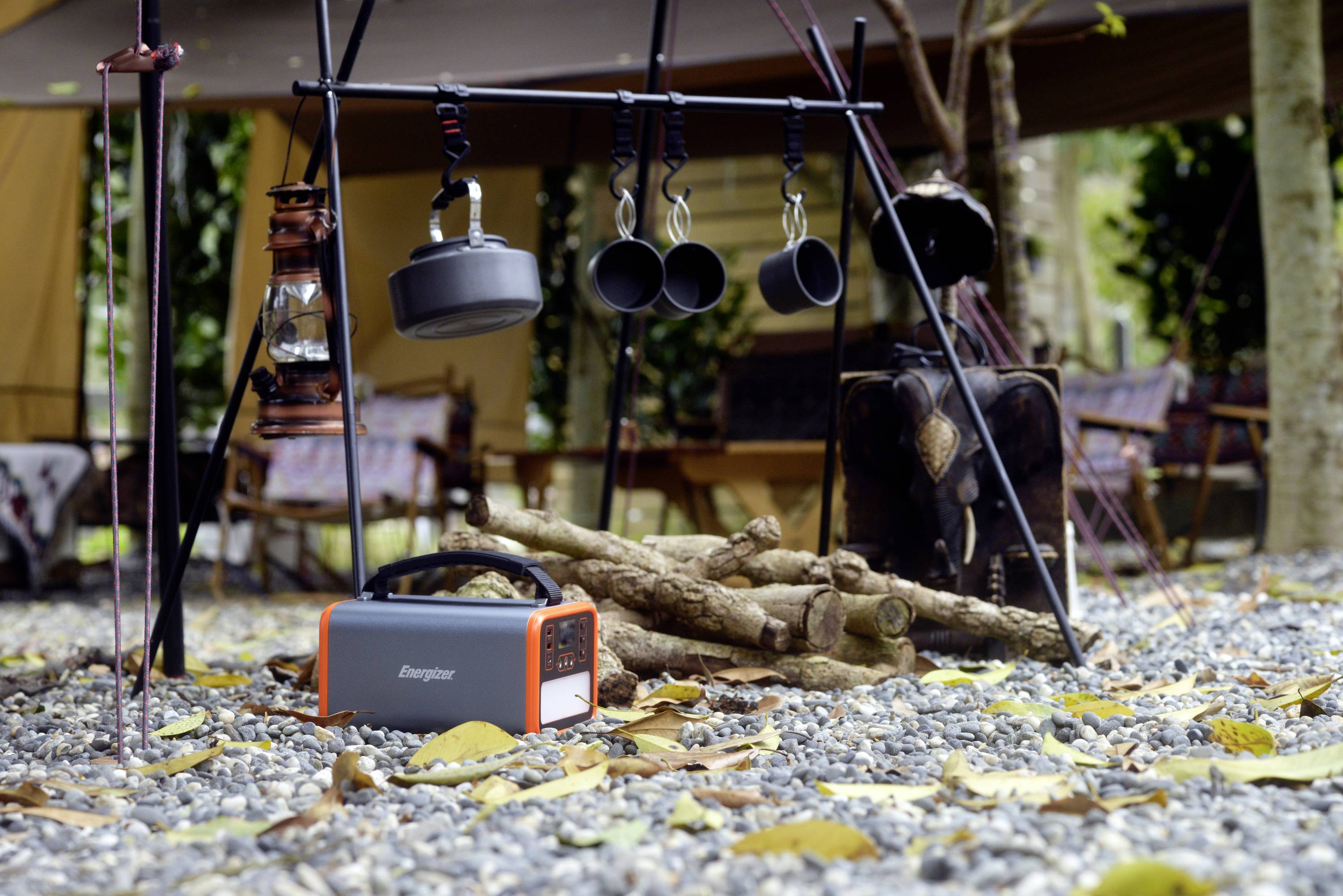 Campeggio con set da cucina sospeso, lanterna e fonte di energia portatile su un terreno sassoso in un ambiente boschivo.