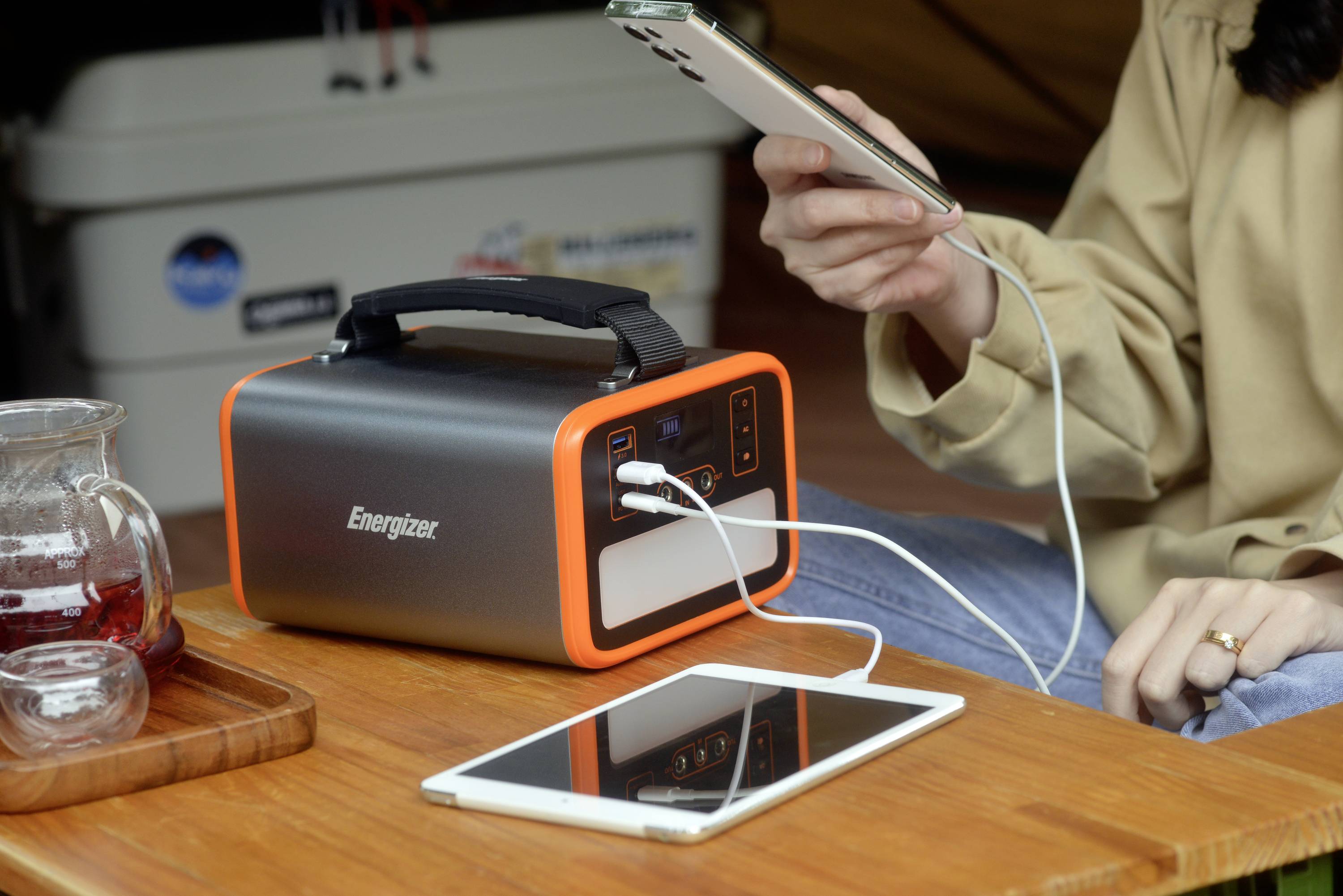 Una persona sta caricando uno smartphone e un tablet con un caricabatterie portatile Energizer, posizionato su un tavolo di legno.