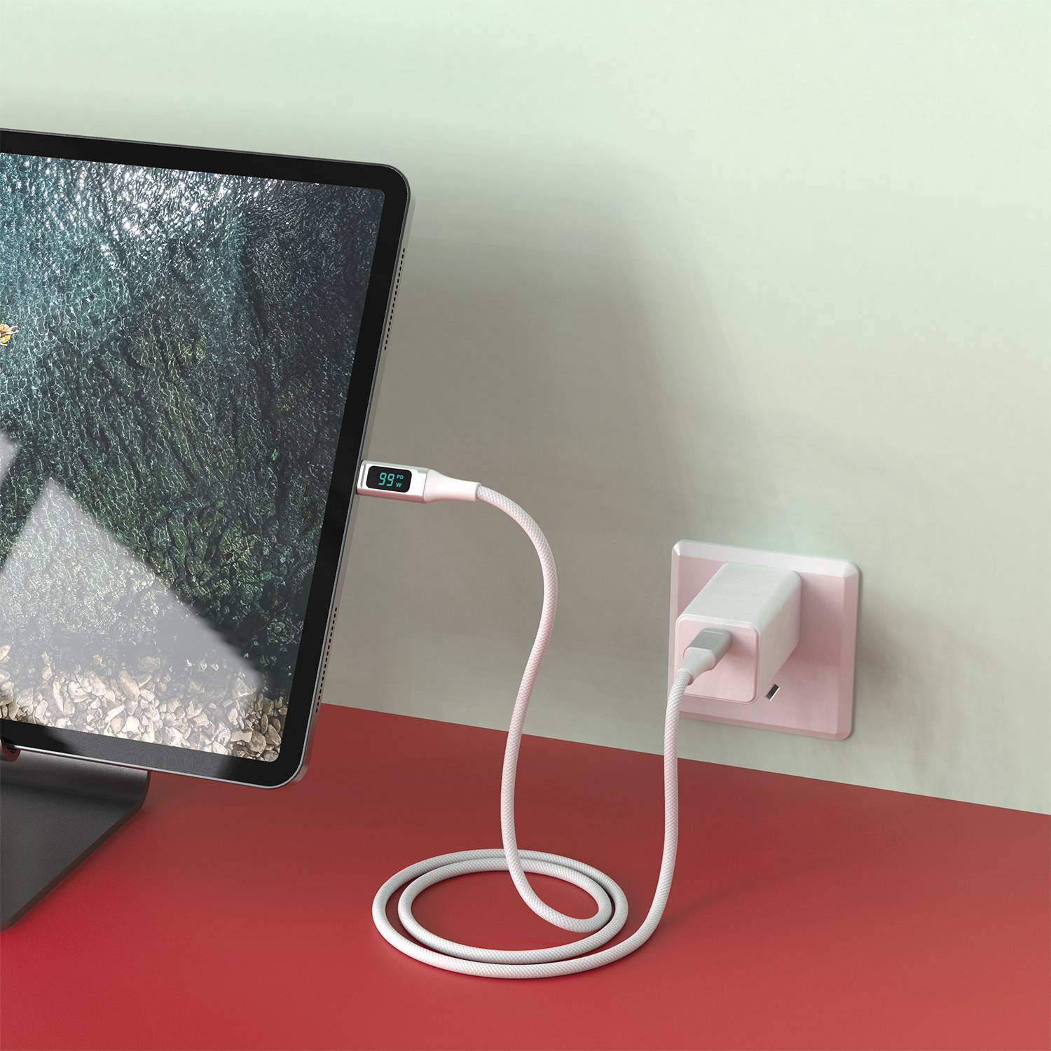Un monitor mostra un paesaggio verde. Un cavo di ricarica è collegato alla presa a muro, e il display indica '99%'.