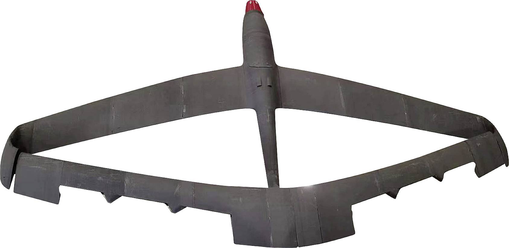 Un prototipo di drone nero, simile a un aereo, con ali larghe e punta rossa, fotografato dal basso.