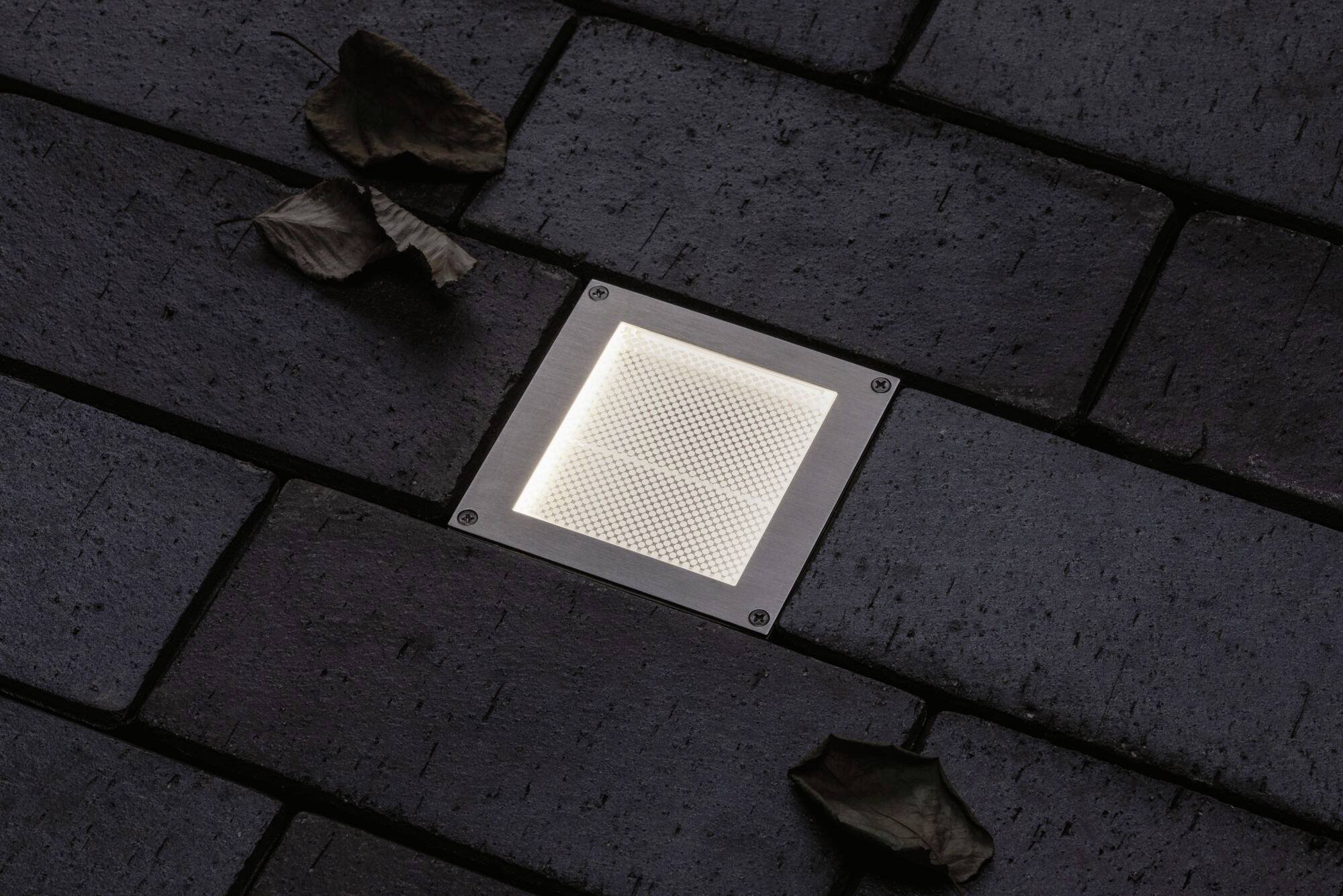 Mattonelle con illuminazione a pavimento integrata e due foglie secche ai bordi.