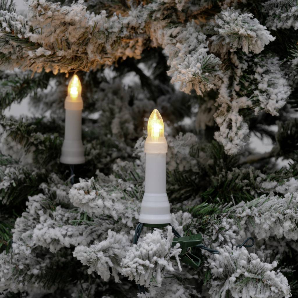Due candele luminose bianche pendono da un ramo di abete coperto di neve.
