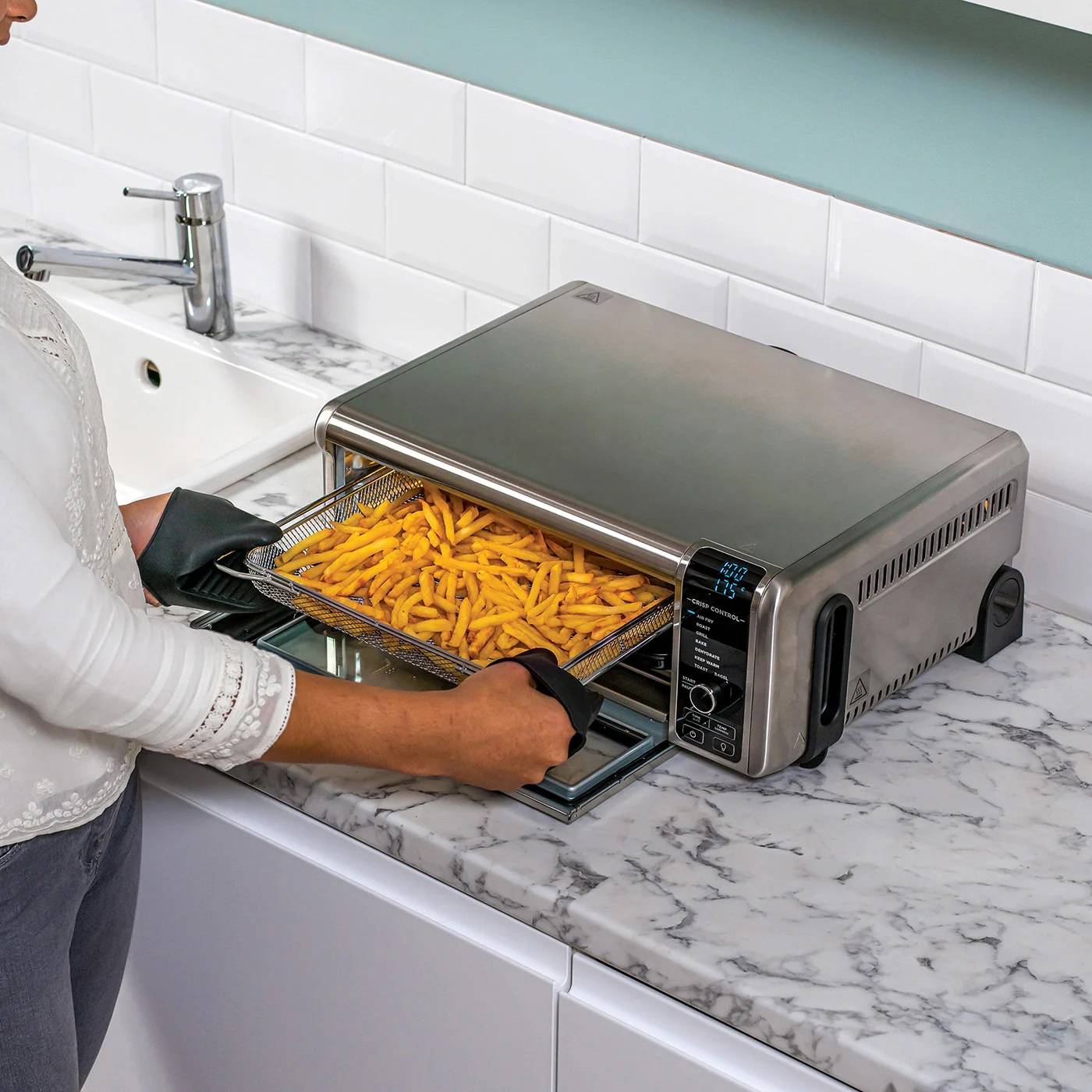 Una persona sta prelevando patatine fritte croccanti da un cestello di una friggitrice ad aria in una cucina moderna.