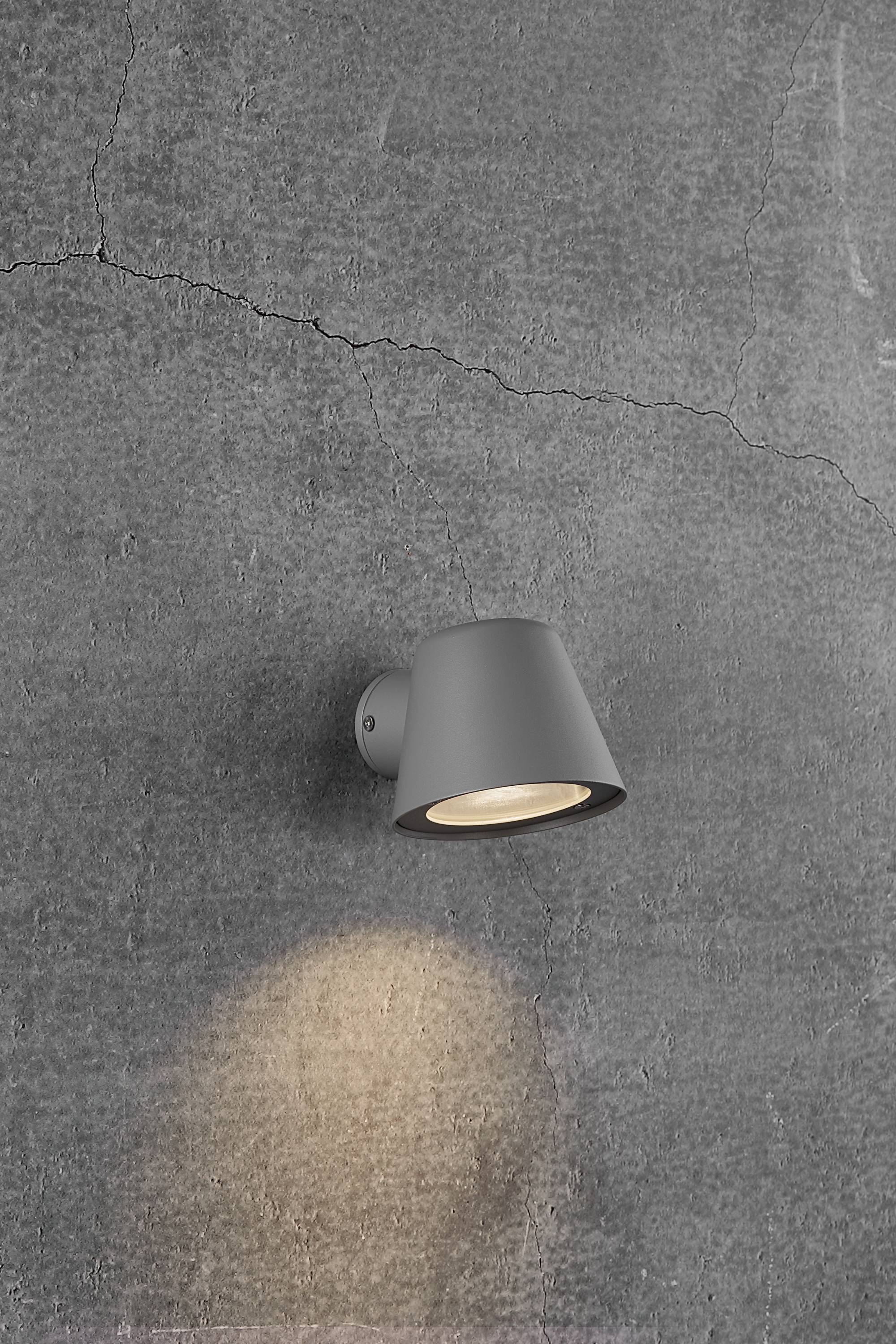 Una lampada da parete grigia irradia una luce calda su una parete grigia con texture.