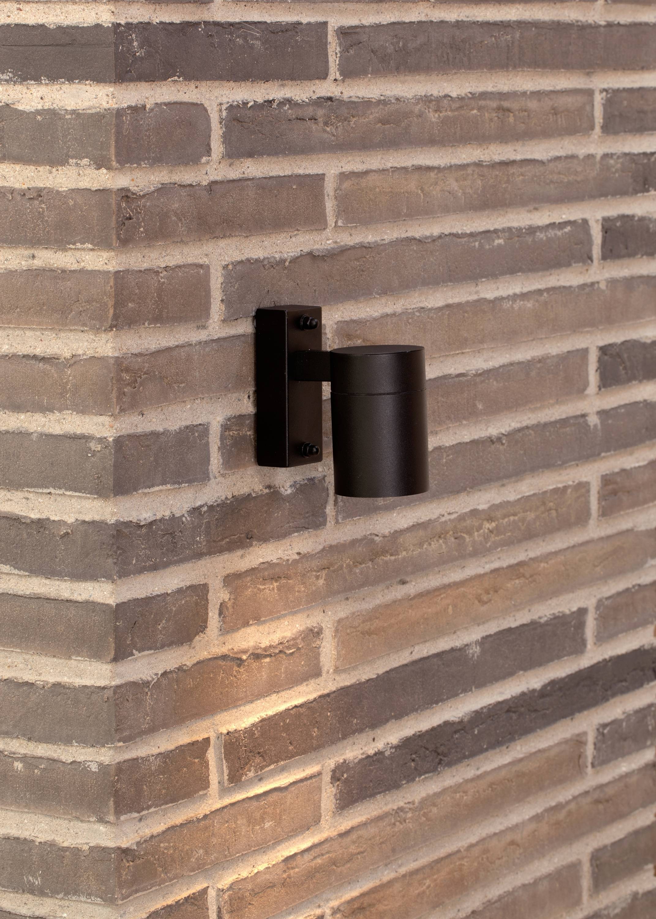 Applique esterna nera su un muro di mattoni, illumina l'area sottostante.