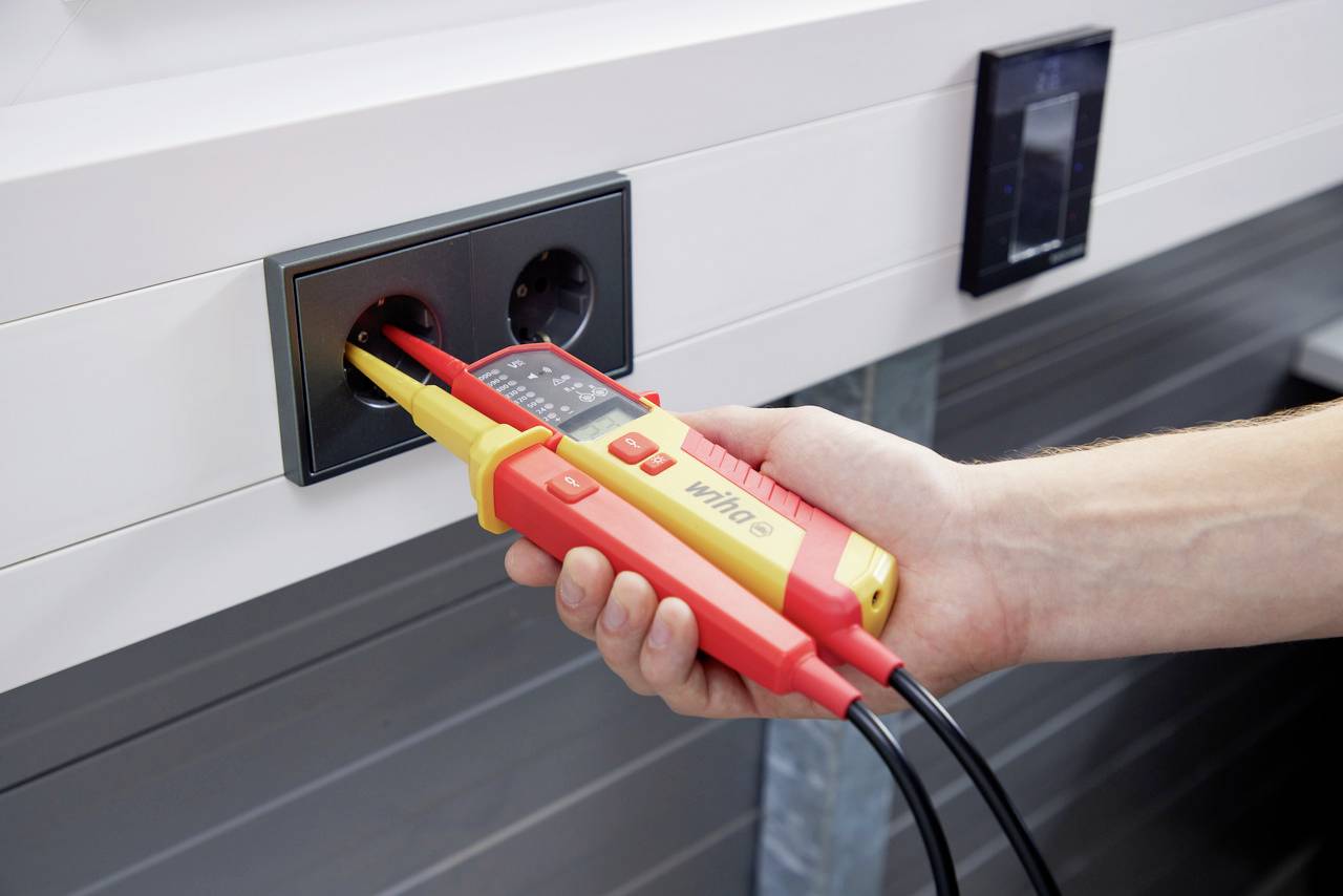 Una mano sta utilizzando un tester per verificare la tensione di una presa a muro.