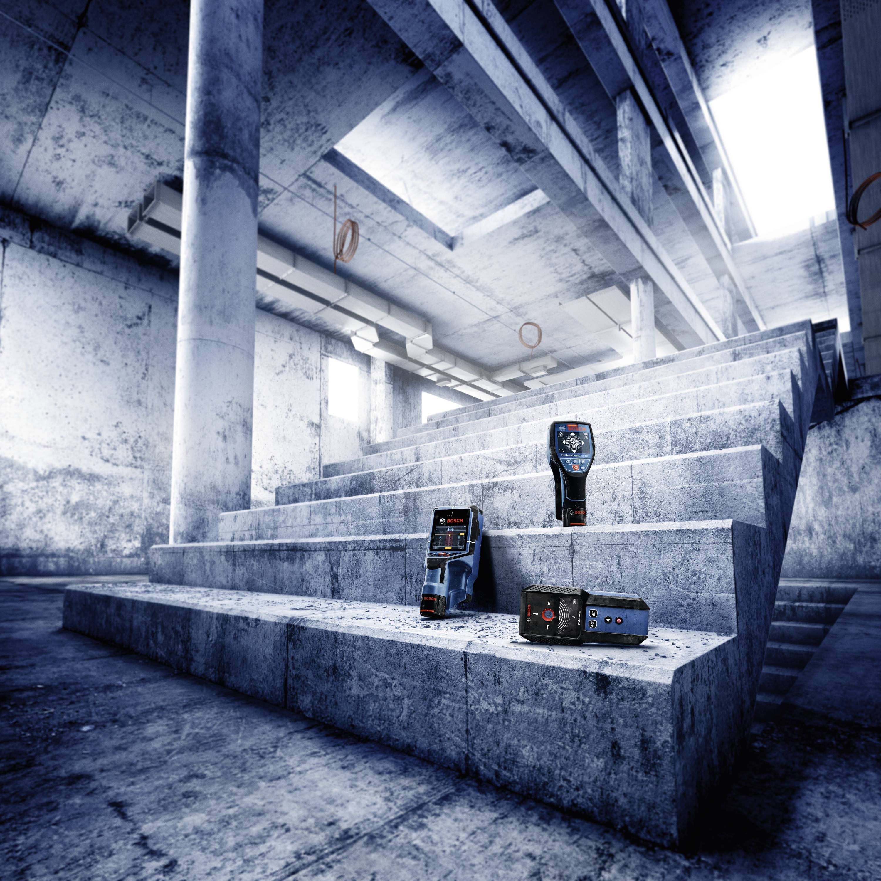Un vano scale moderno con pareti in calcestruzzo strutturate. Sui gradini sono posizionati tre diversi strumenti tecnici per il rilievo.