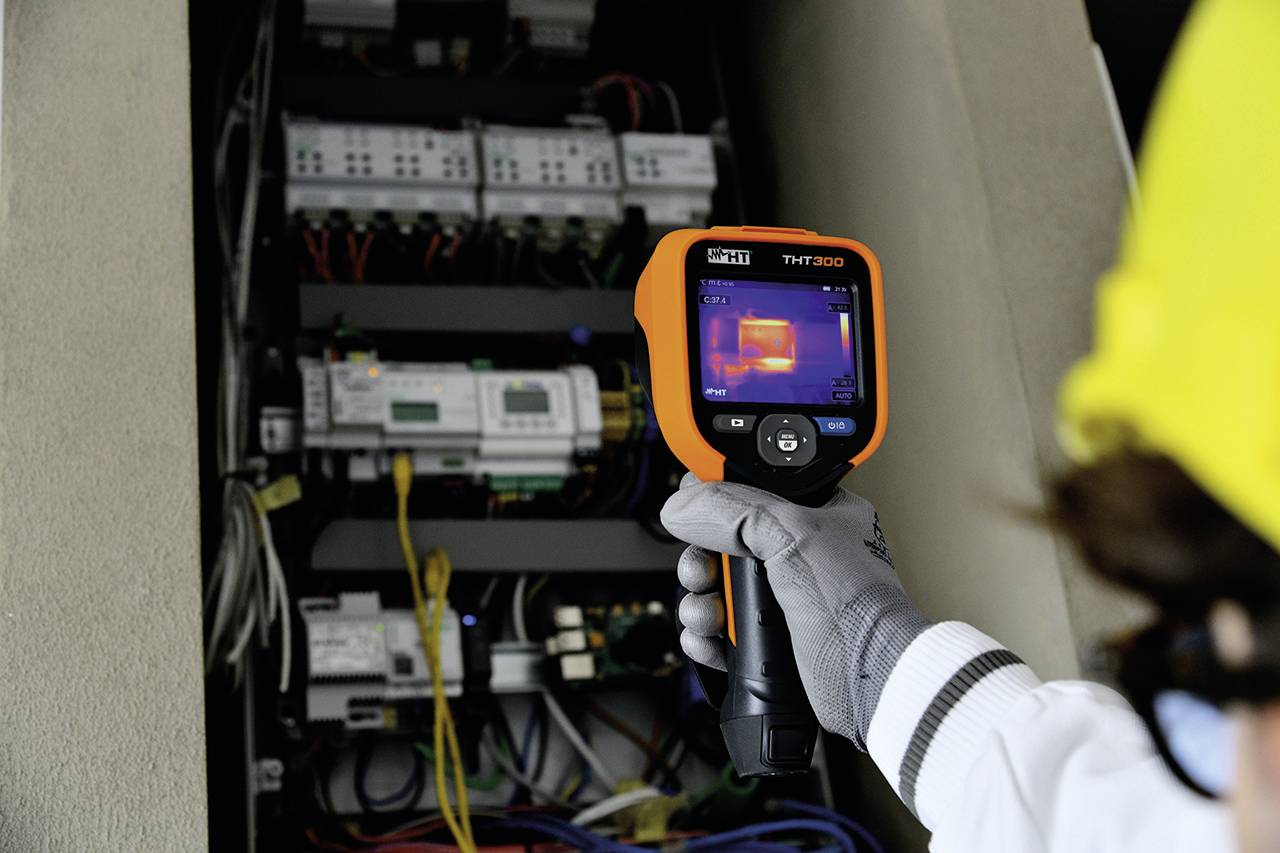 Una persona utilizza una termocamera per controllare la temperatura di un quadro elettrico.