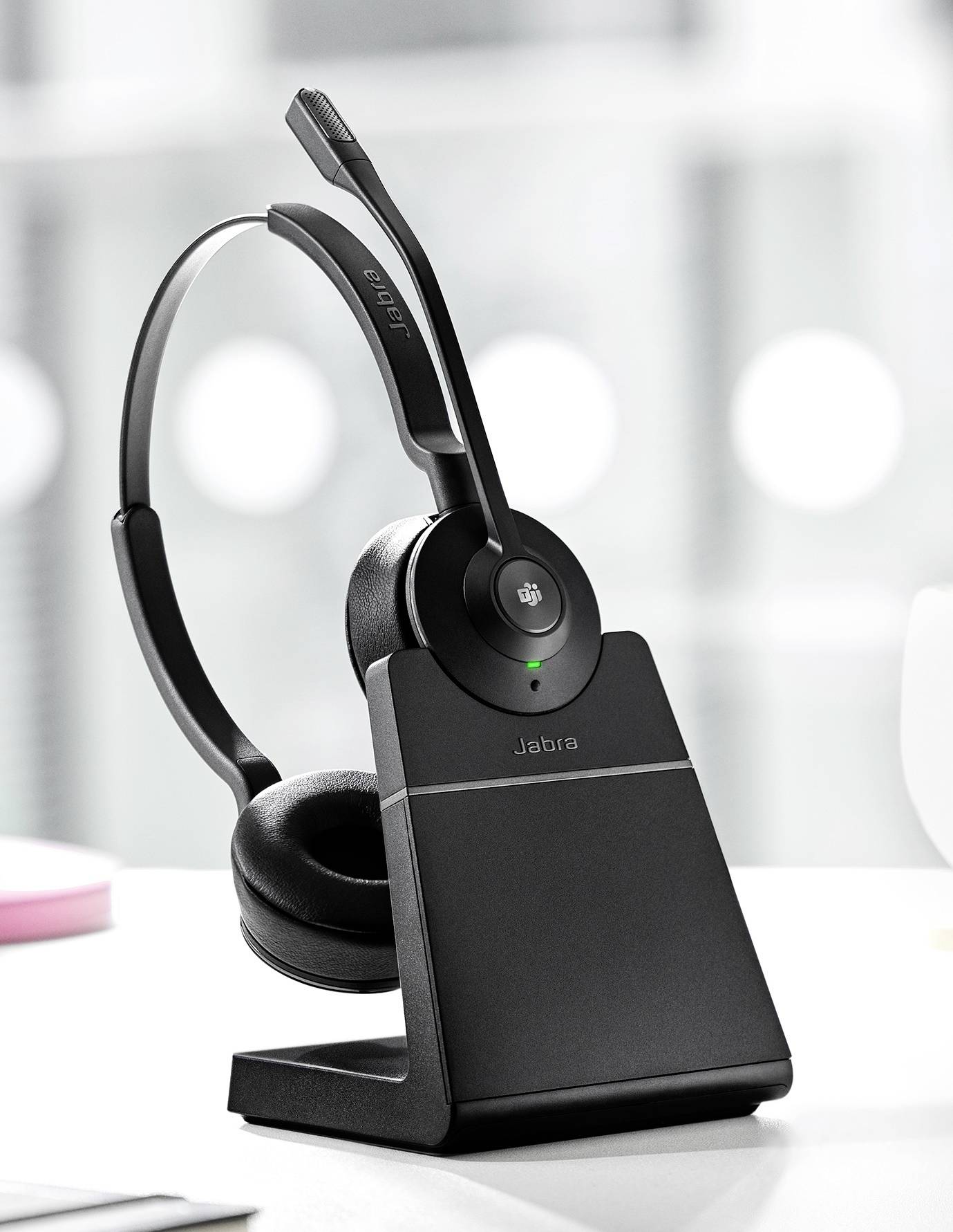Cuffie wireless su stazione di ricarica, adatte per ambienti d'ufficio, con braccio microfono, che mostrano un design moderno in tono neutro.