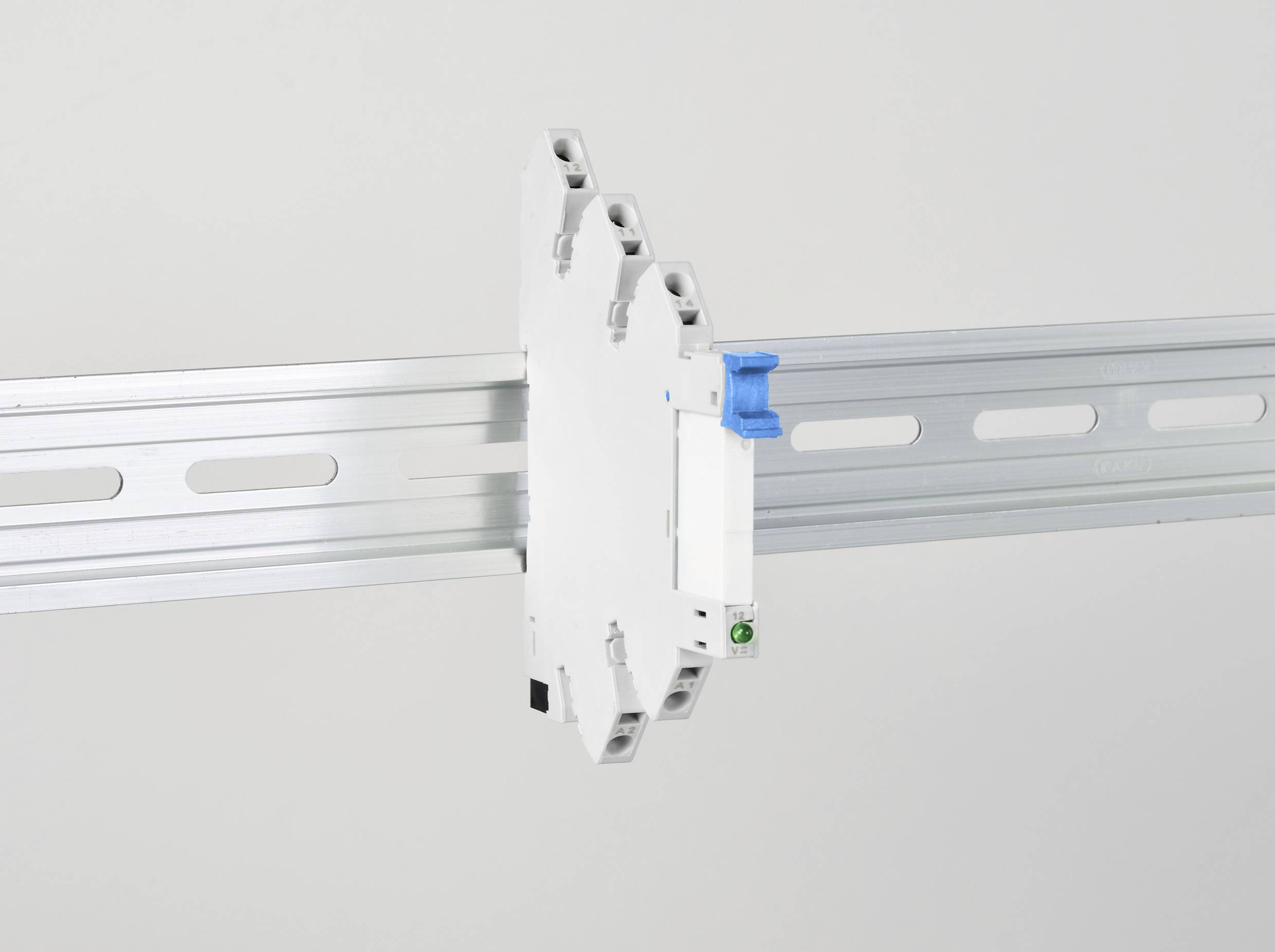 Un dispositivo elettrico bianco con un componente blu è montato su una guida metallica grigia. È destinato all'installazione in quadri elettrici.