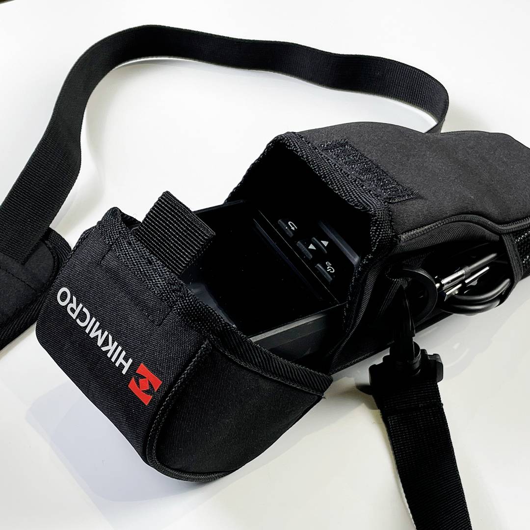 Una borsa nera per fotocamera con la scritta 'Himacro', contiene una macchina fotografica ed è dotata di una tracolla, poggiata su uno sfondo bianco.