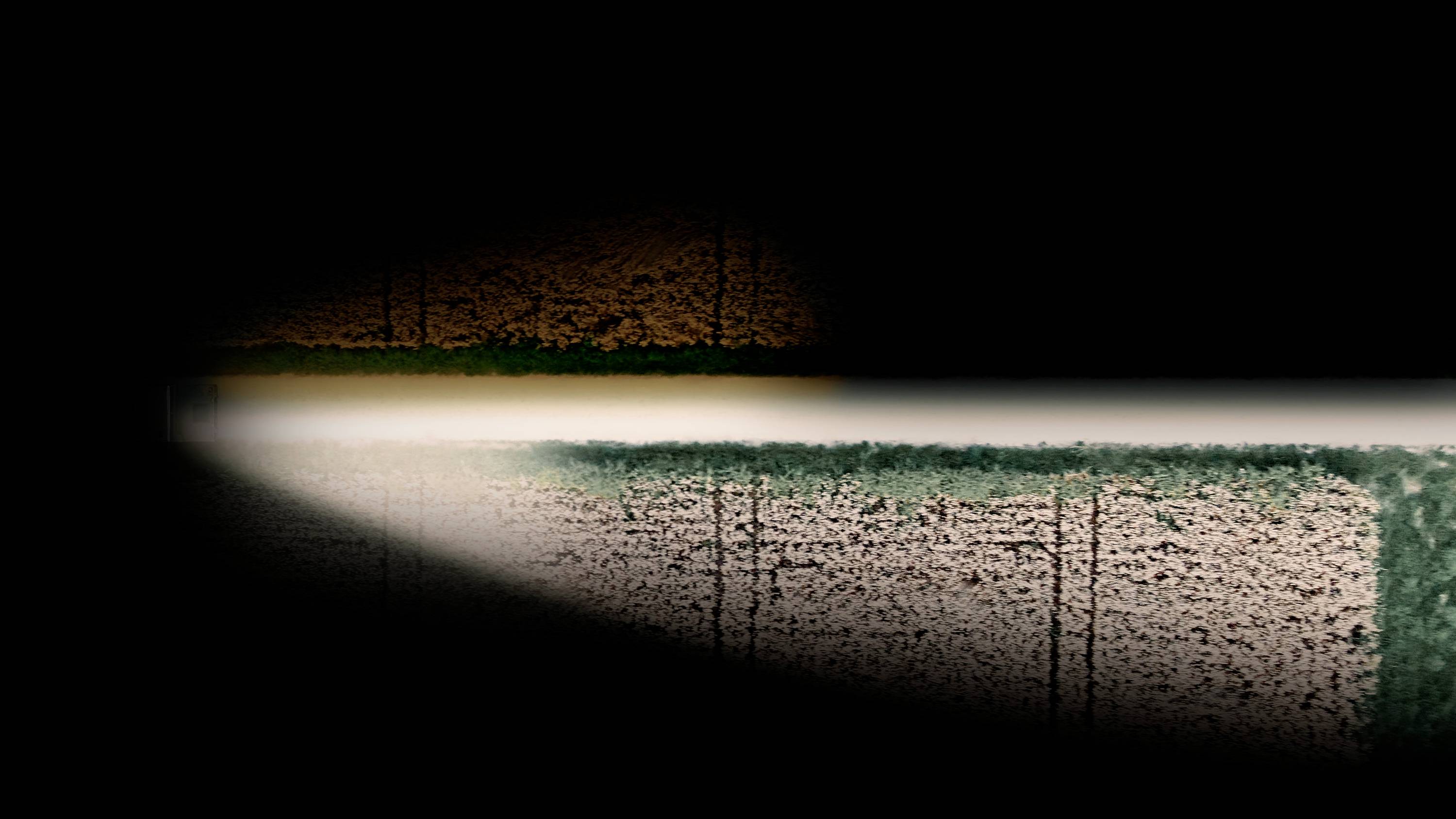 Paesaggio cupo con un sottile raggio di luce che illumina una stretta sezione di terreno con erba e terra.