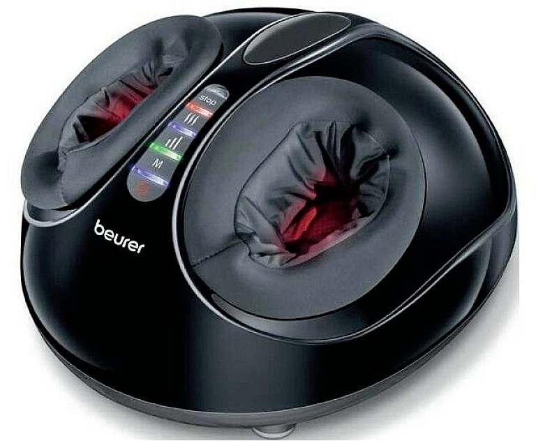 Dispositivo nero per massaggio shiatsu ai piedi con due aperture imbottite e indicatore LED. Il marchio 'Beurer' è stampato sopra.