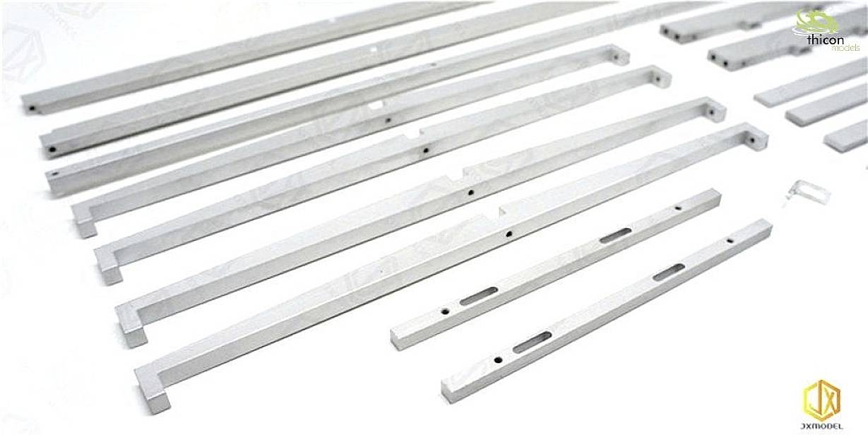 Diversi profili metallici di varie lunghezze sono disposti fianco a fianco su una superficie bianca, probabilmente componenti per un involucro.