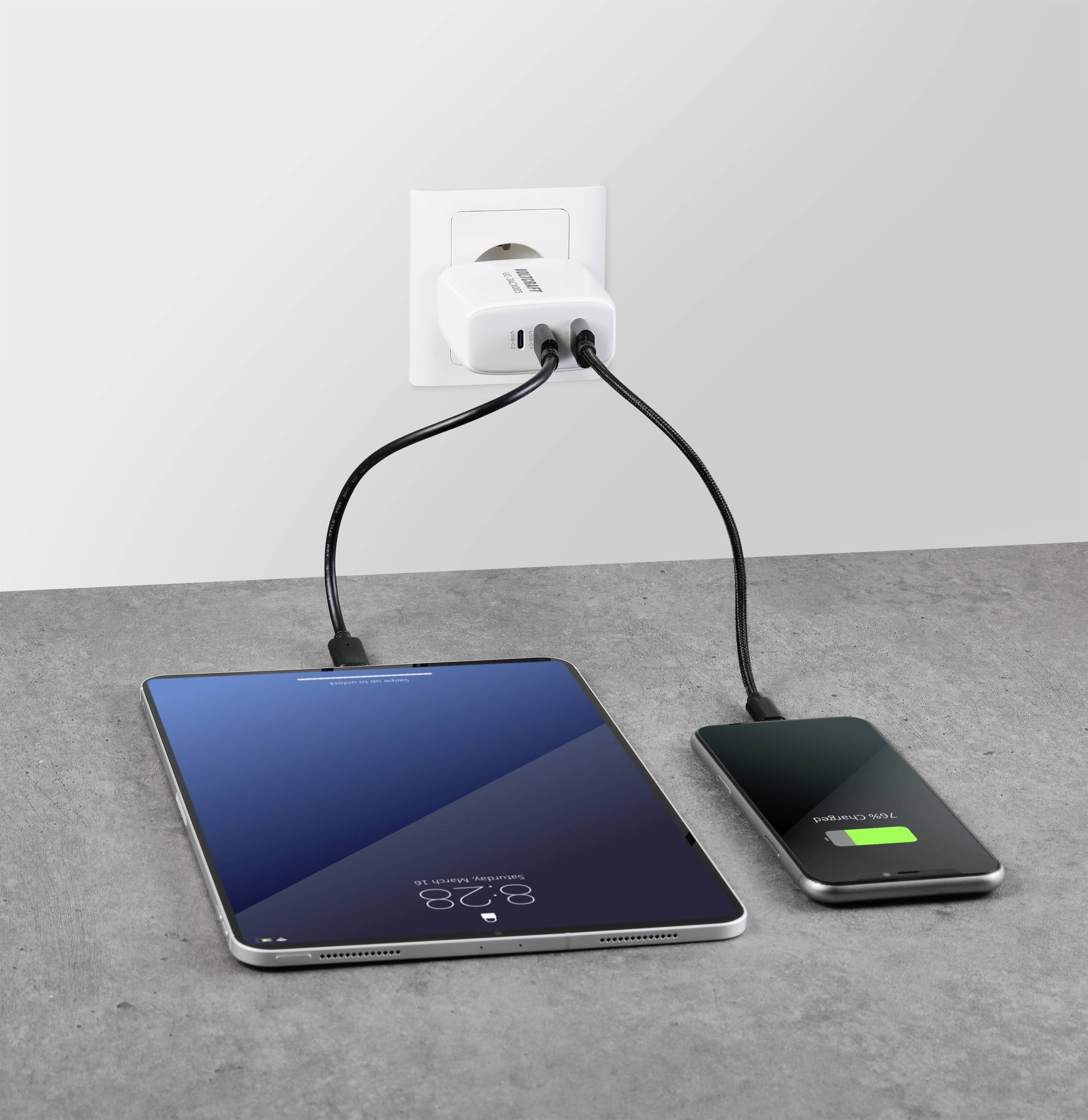 Un tablet e uno smartphone vengono caricati contemporaneamente a una presa elettrica. Lo smartphone mostra una barra di carica verde.