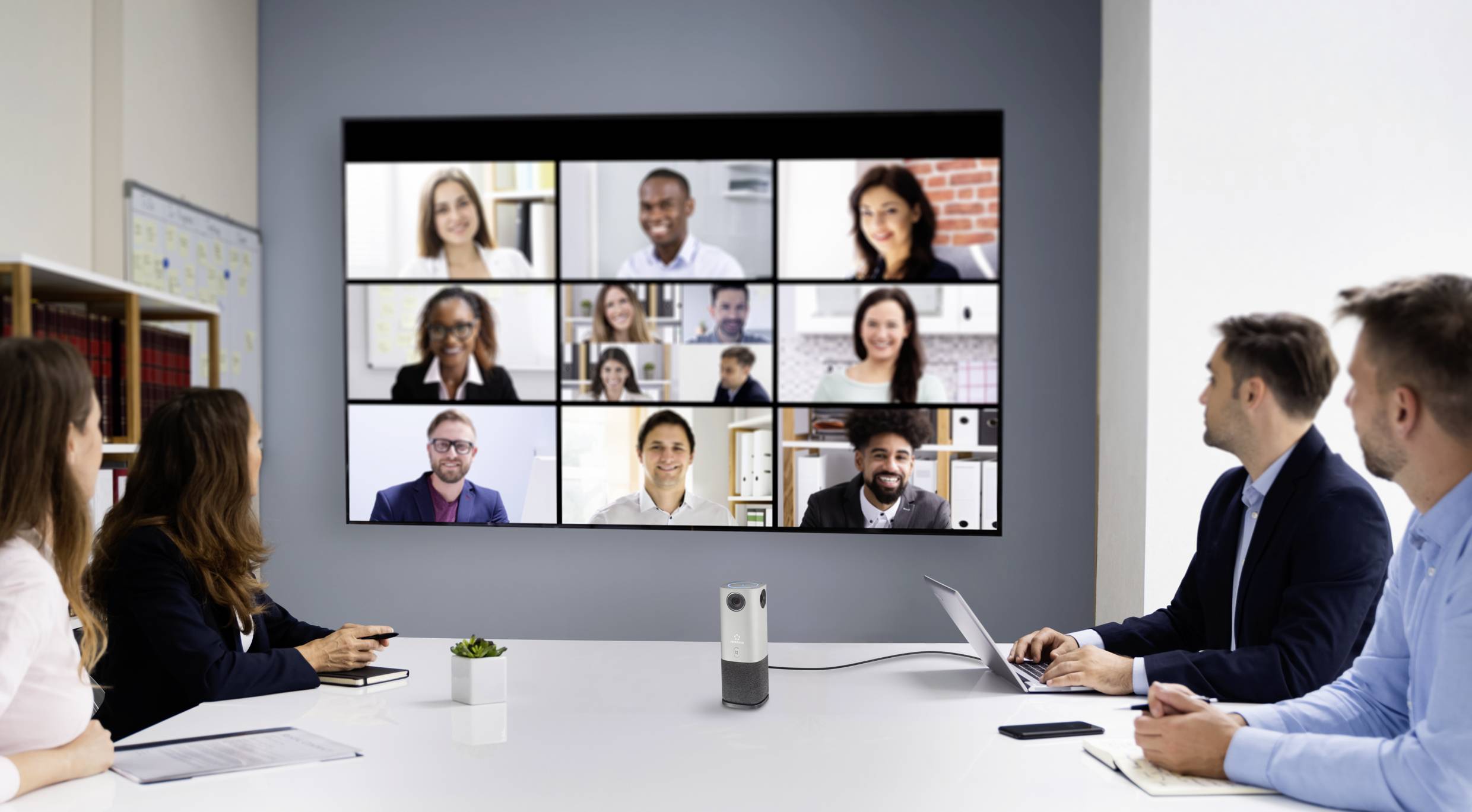 Persone in una sala riunioni stanno conducendo una videoconferenza multipartecipativa su un grande schermo.