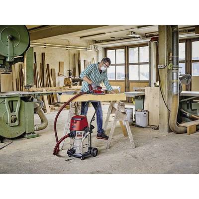 Una persona sta lavorando in una falegnameria con un pialla elettrica per levigare una tavola di legno. Sullo sfondo si vedono macchine e scorte di legno.
