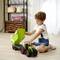 Un bambino gioca in soggiorno con un trattore giocattolo verde con rimorchio. Sullo sfondo si vedono degli scaffali con oggetti decorativi.