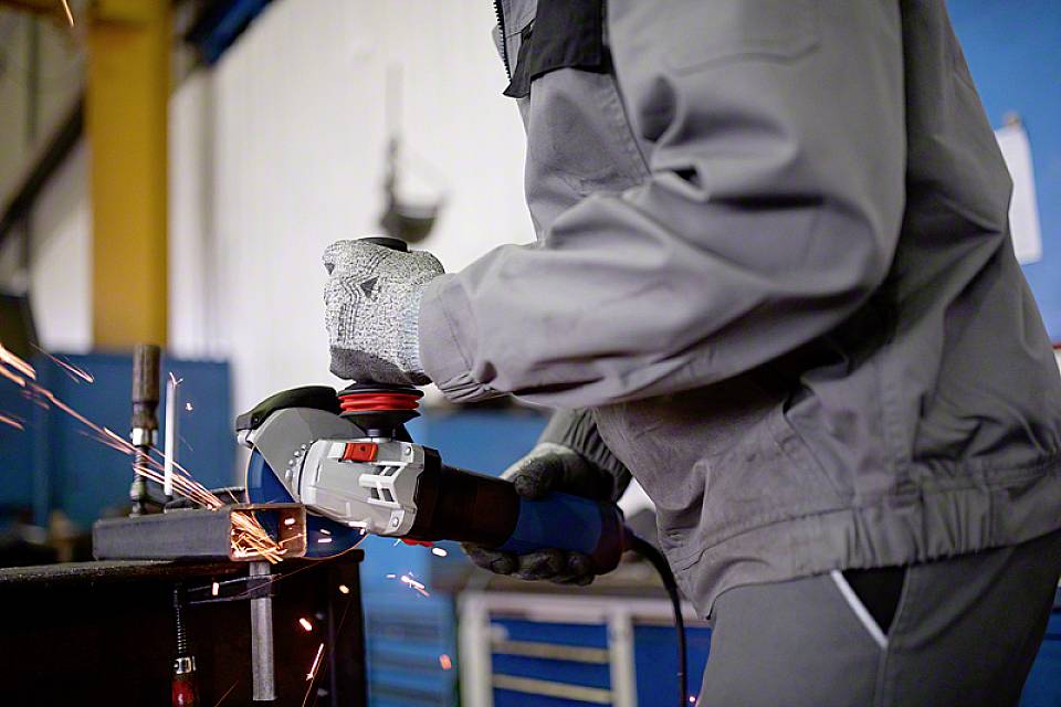 Una persona in abbigliamento da lavoro sta levigando il metallo con un smerigliatrice angolare, mentre scintille volano. La scena mostra un lavoro artigianale in un laboratorio.