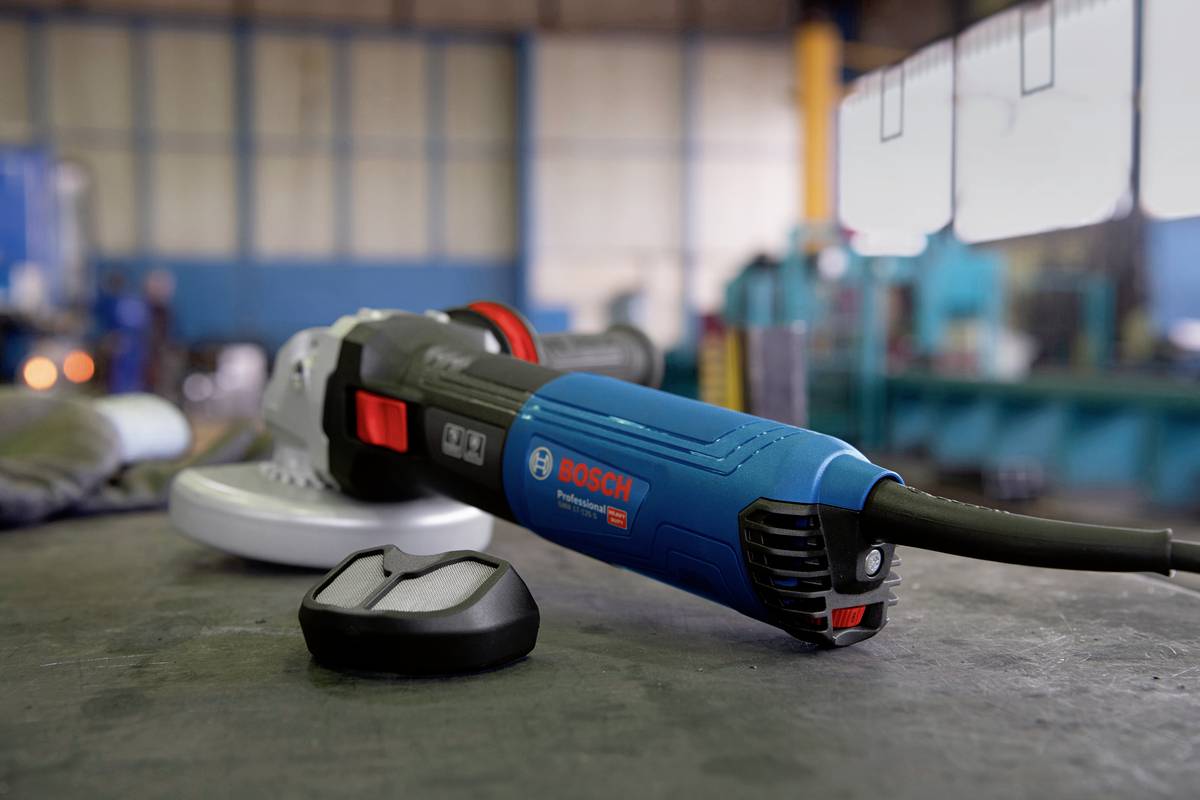 Un smerigliatrice angolare blu è posizionata su un tavolo in un laboratorio. Accanto a sinistra c'è un pezzo di metallo. Sullo sfondo, macchine sfocate.