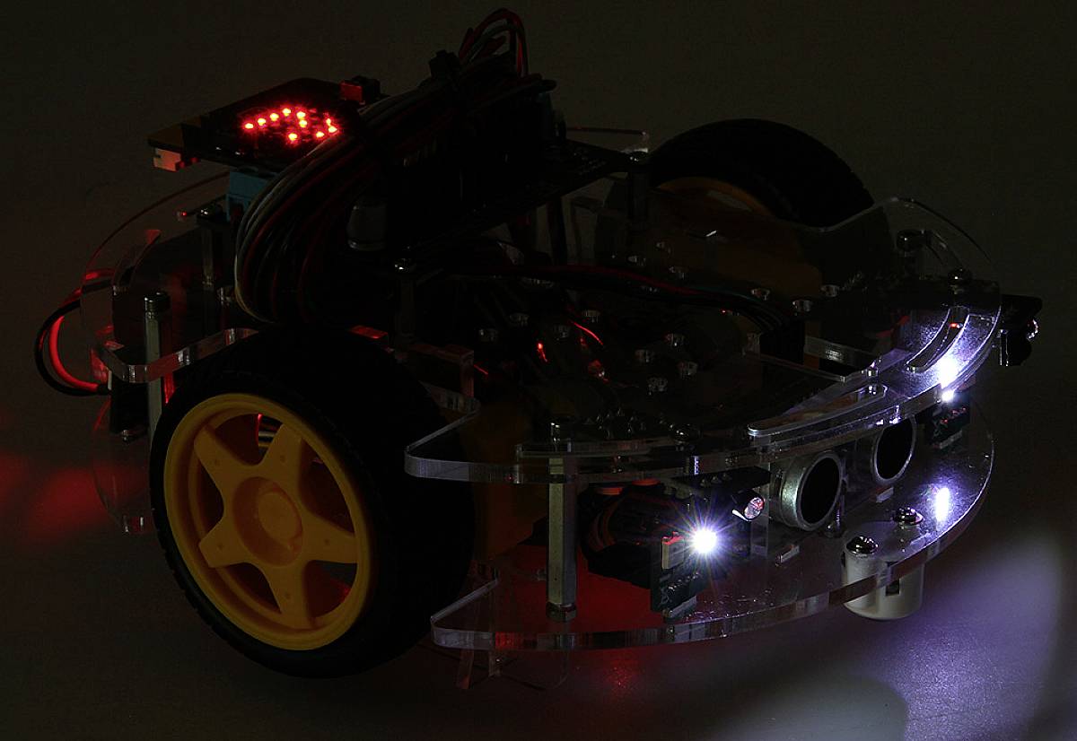 Un piccolo robot con ruote gialle su una superficie scura. Ha diversi LED e cavi visibili sulla parte superiore.