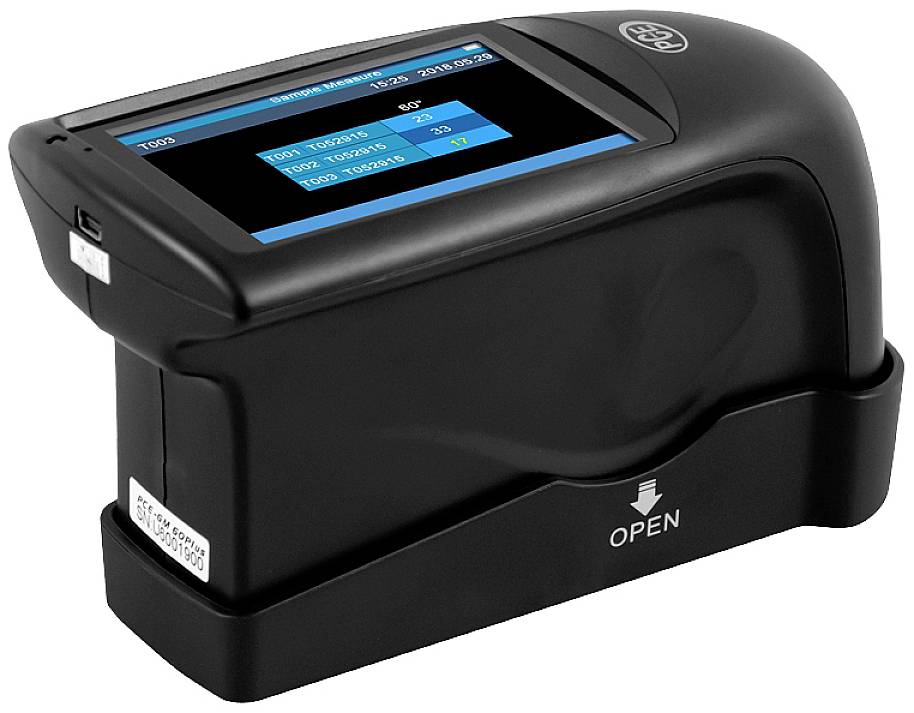 Un dispositivo portatile nero con display digitale mostra valori di misurazione e la data. È posizionato in un supporto contrassegnato con la scritta 'OPEN'.