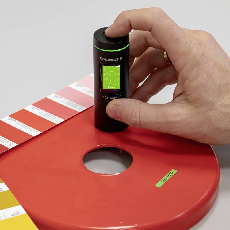 Una mano tiene un colorimetro poggiato su una carta campione dei colori. Il colorimetro mostra valori utilizzati per la misurazione del colore.
