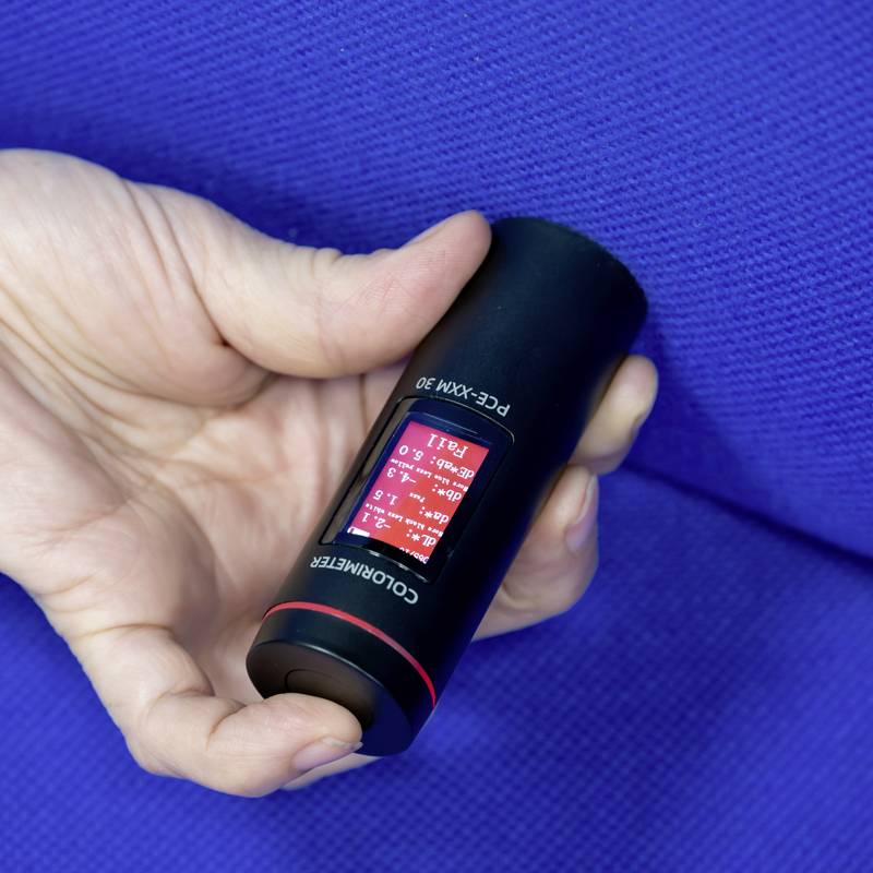 Una mano tiene un dispositivo nero a forma di cilindro con display digitale e sfondo rosso che mostra valori di temperatura. Sullo sfondo, colore blu.