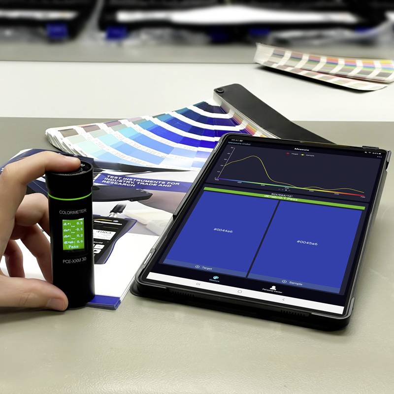 Una mano tiene un colorimetro accanto a un tablet. Sul tablet viene visualizzato un diagramma di misurazione del colore. Ventagli di campioni colore sullo sfondo.