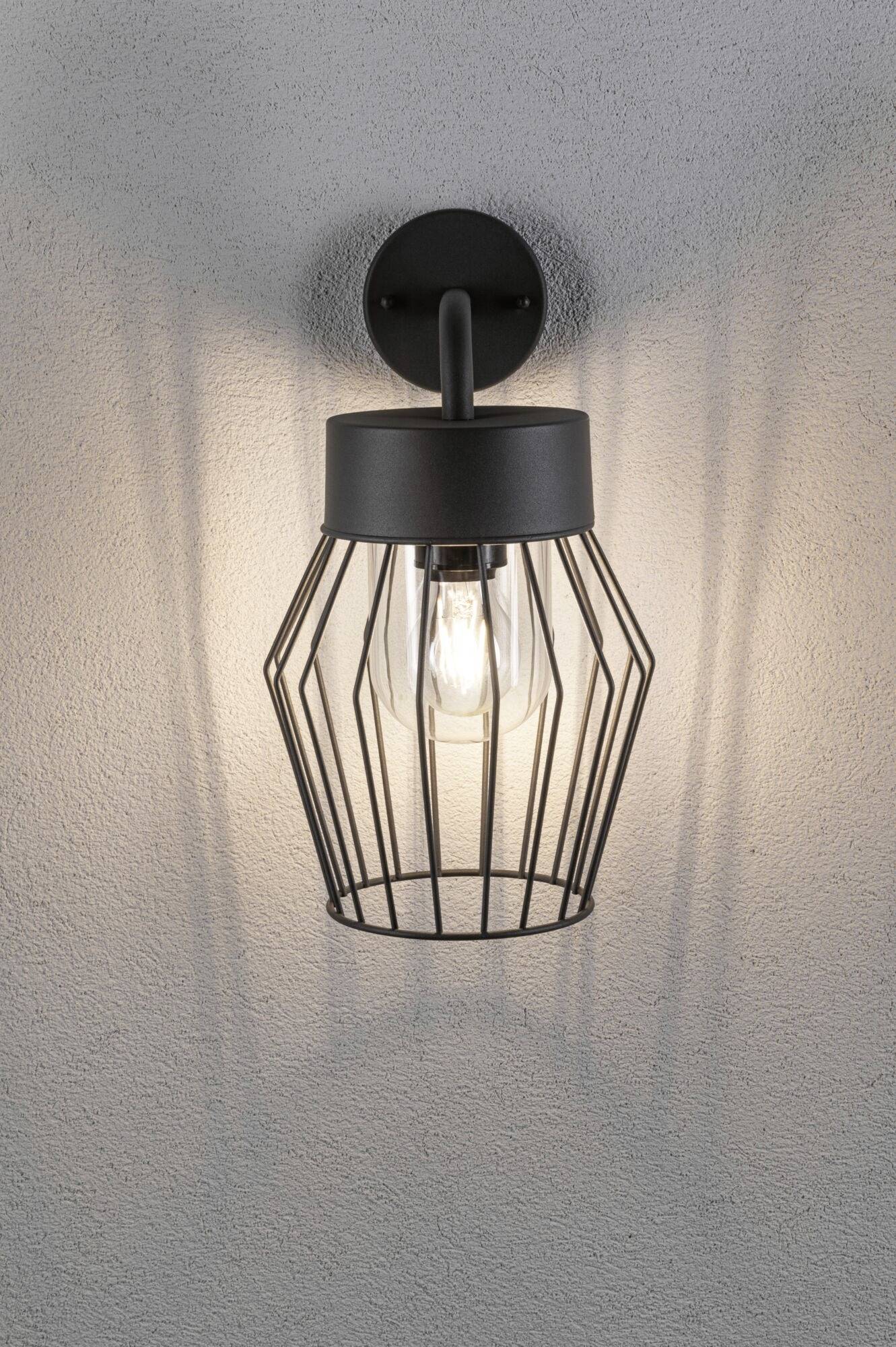 Una lampada da parete elegante in metallo nero a forma di lanterna che proietta una luce soffusa verso l'alto e il basso su una parete grigia.