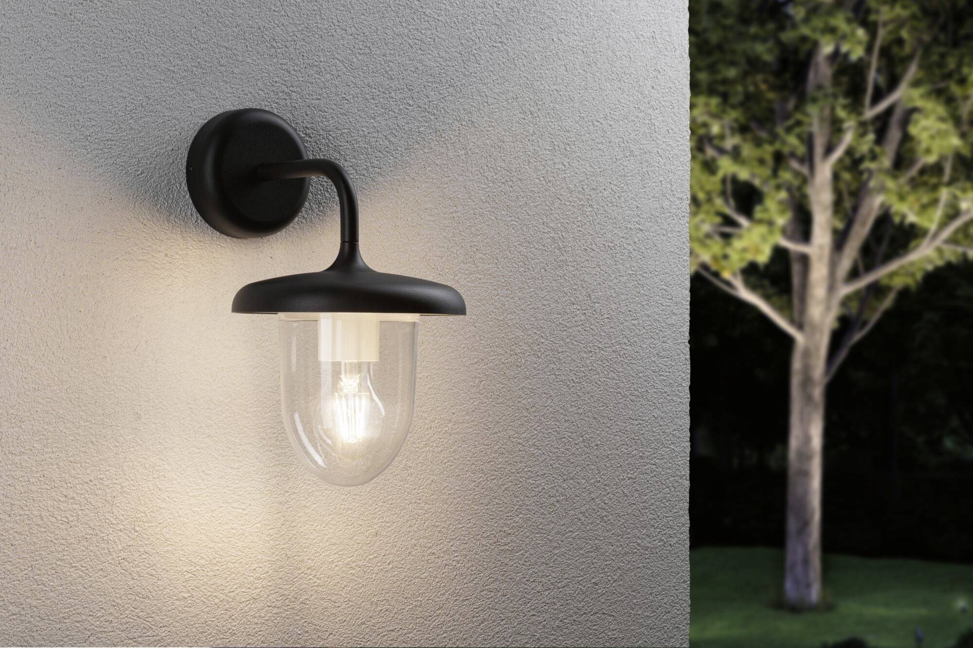 Lampada da parete montata su un muro che illumina nell'oscurità. Sullo sfondo, un albero è visibile nel giardino notturno.