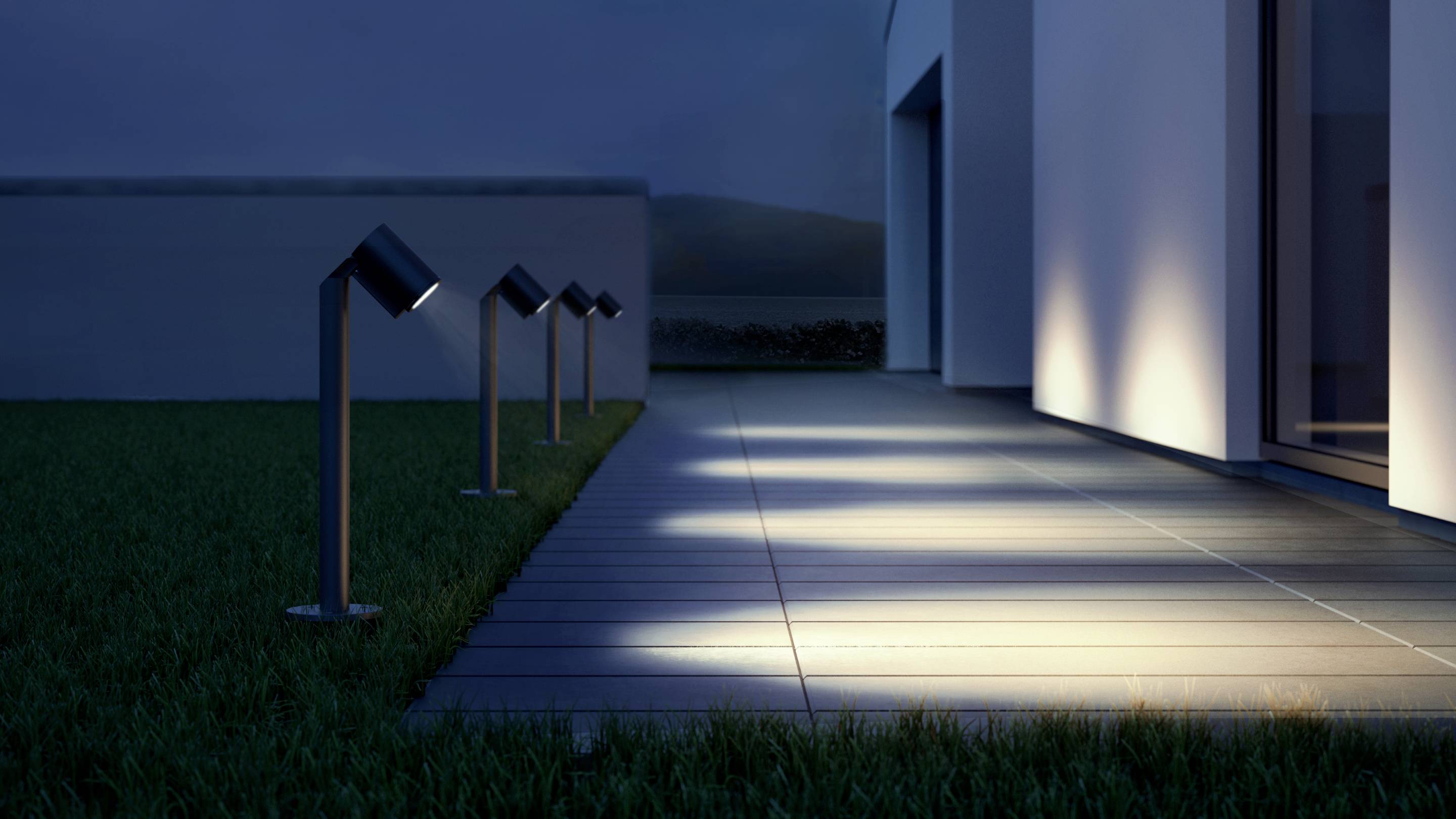 Marciapiede illuminato davanti a un edificio moderno di notte, con diverse luci a pavimento disposte in modo uniforme e regolare.