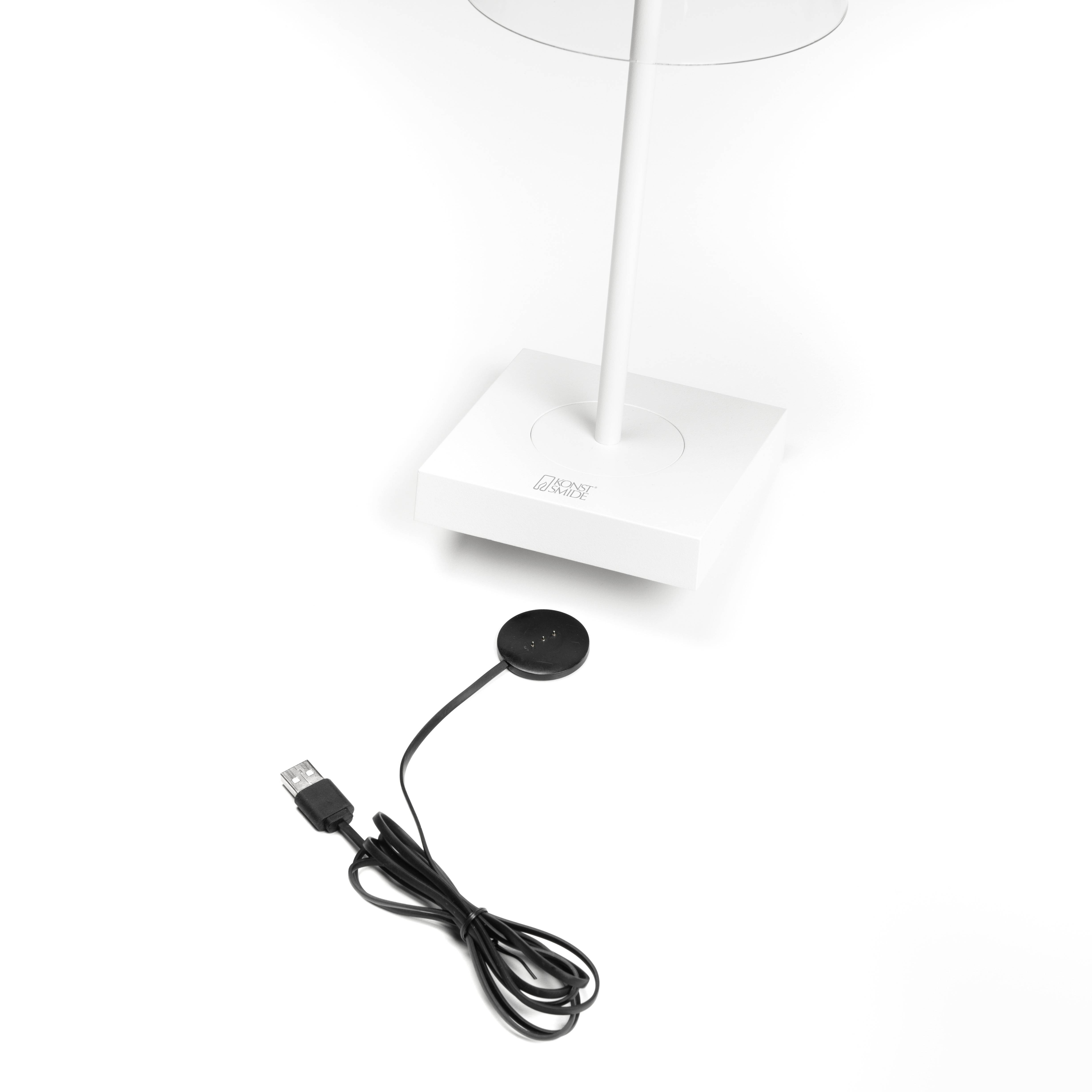 Una lampada da tavolo bianca con base quadrata. Accanto ad essa è posizionato un cavo USB con un dispositivo circolare all'estremità.