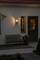 Un ingresso accogliente illuminato di notte, con una panchina e piante accanto alla porta. Una lampada da parete illumina la scena.