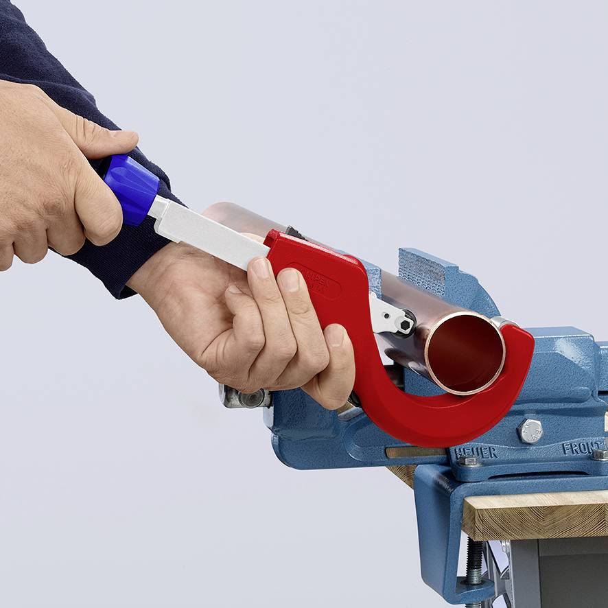 Una persona sta utilizzando un tagliatubi per accorciare un tubo color rame che è fissato in una morsa da banco.