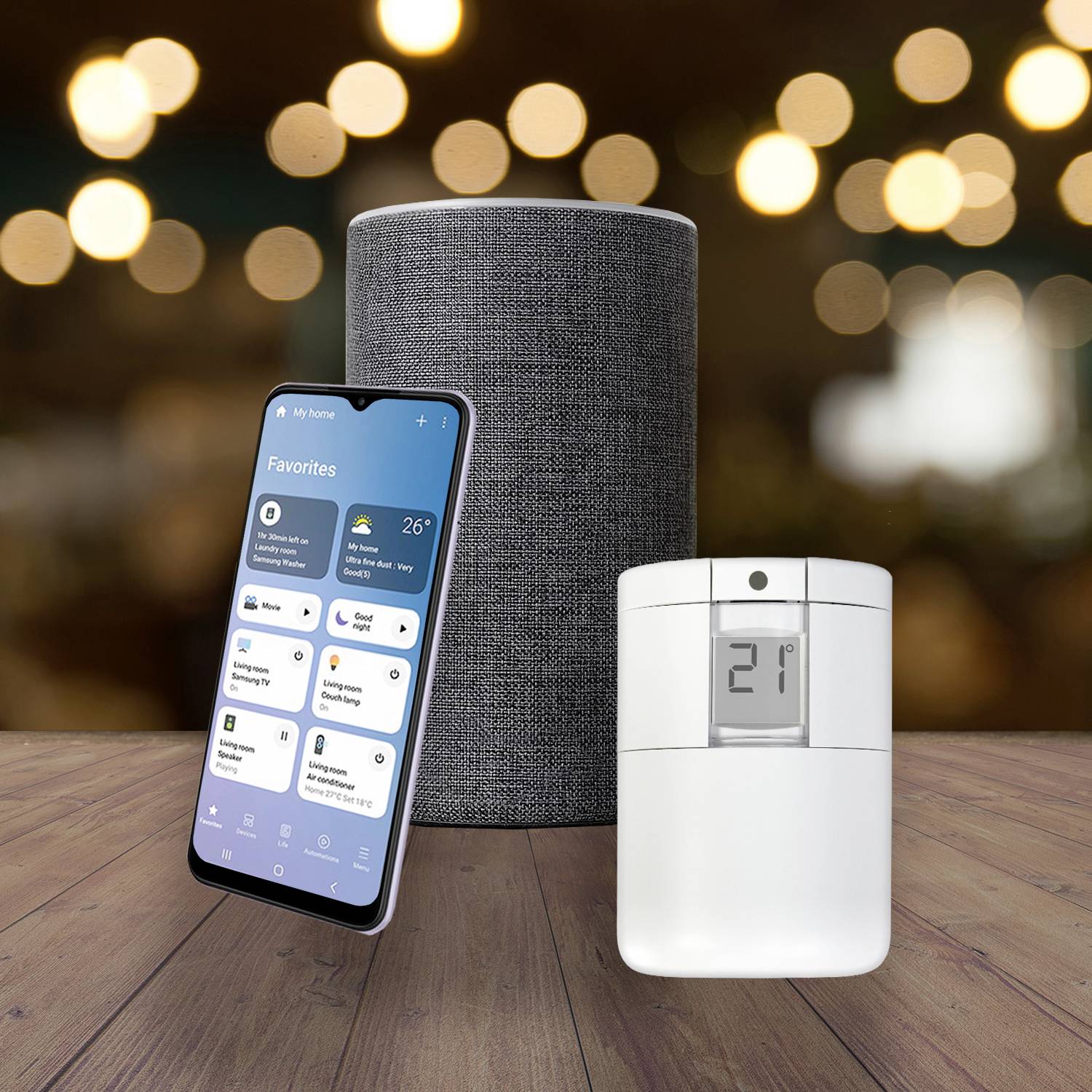 Uno smartphone con un'app per la domotica aperta, un altoparlante intelligente grigio e un termostato digitale che mostra '21' su uno sfondo sfocato.