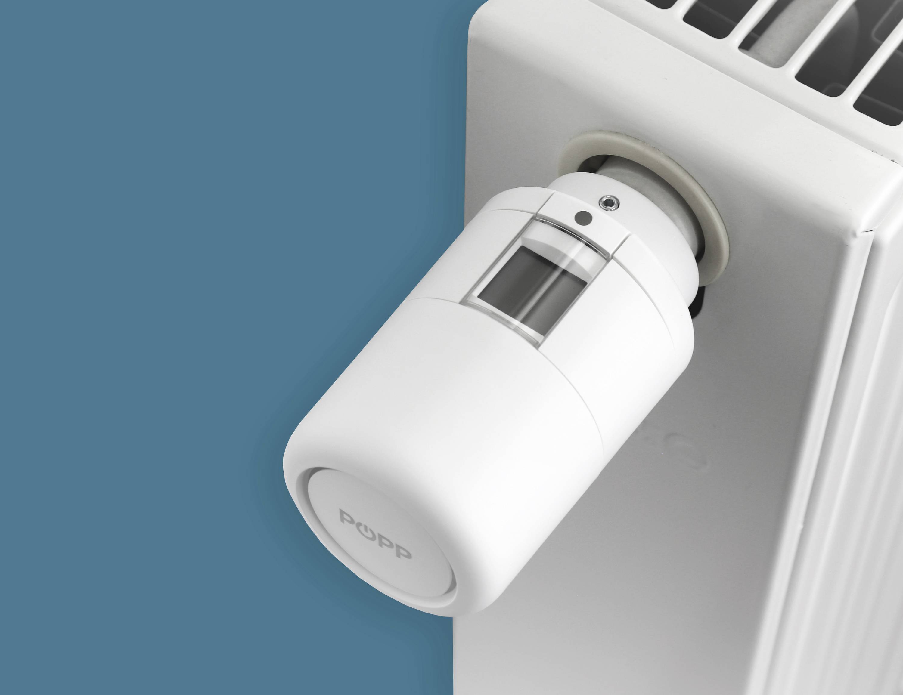 Un termostato digitale bianco per radiatori in primo piano, montato su un radiatore sullo sfondo blu.