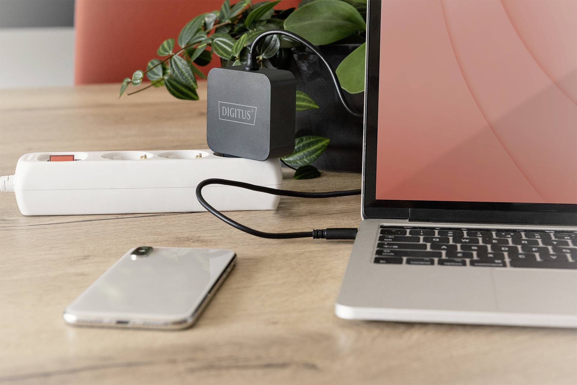 Un laptop su un tavolo è collegato a un caricabatterie tramite un cavo USB. Accanto ci sono uno smartphone e una presa multipla.
