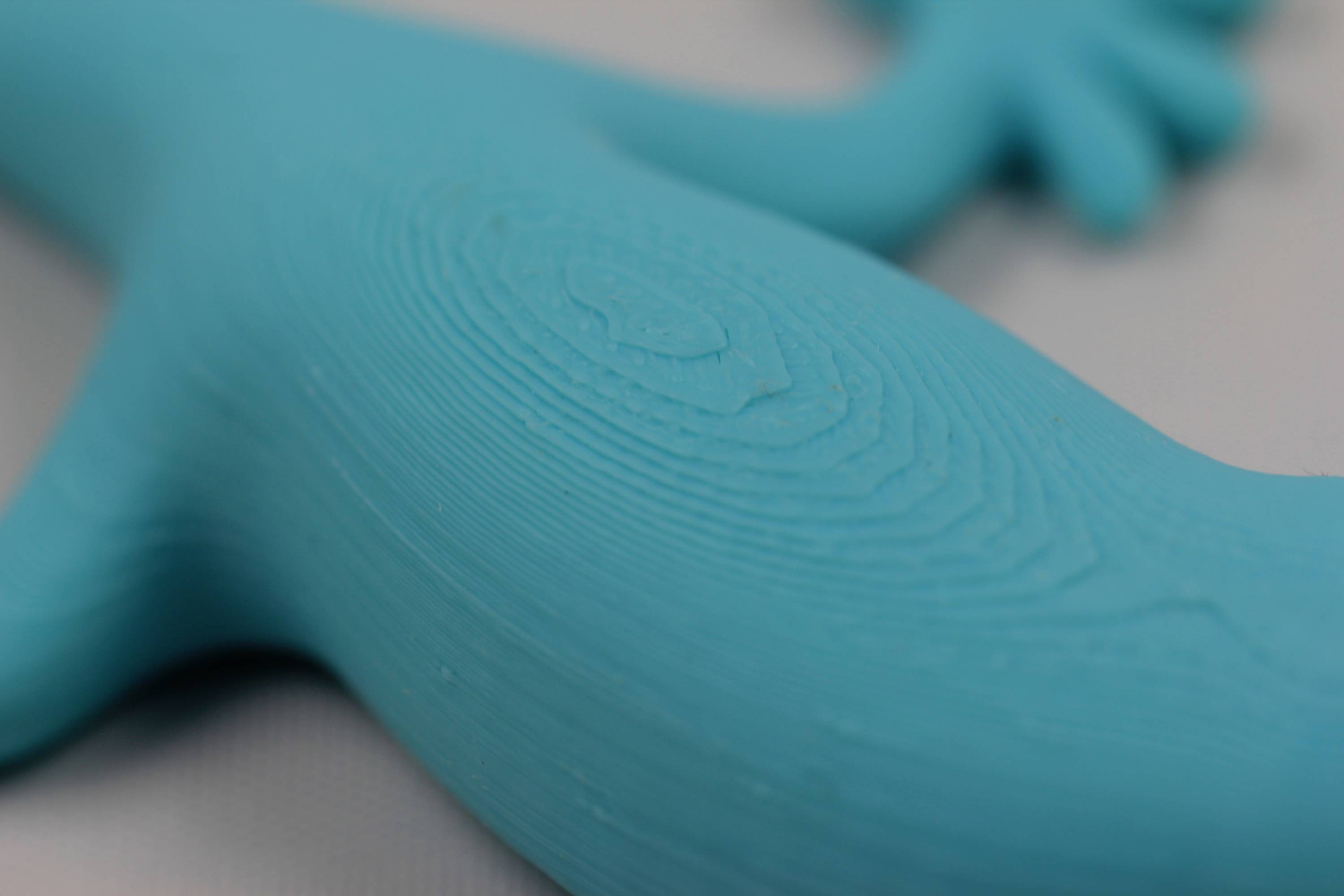 Primo piano di un giocattolo di plastica blu a forma di lucertola. Il materiale mostra sottili linee concentriche sulla superficie.