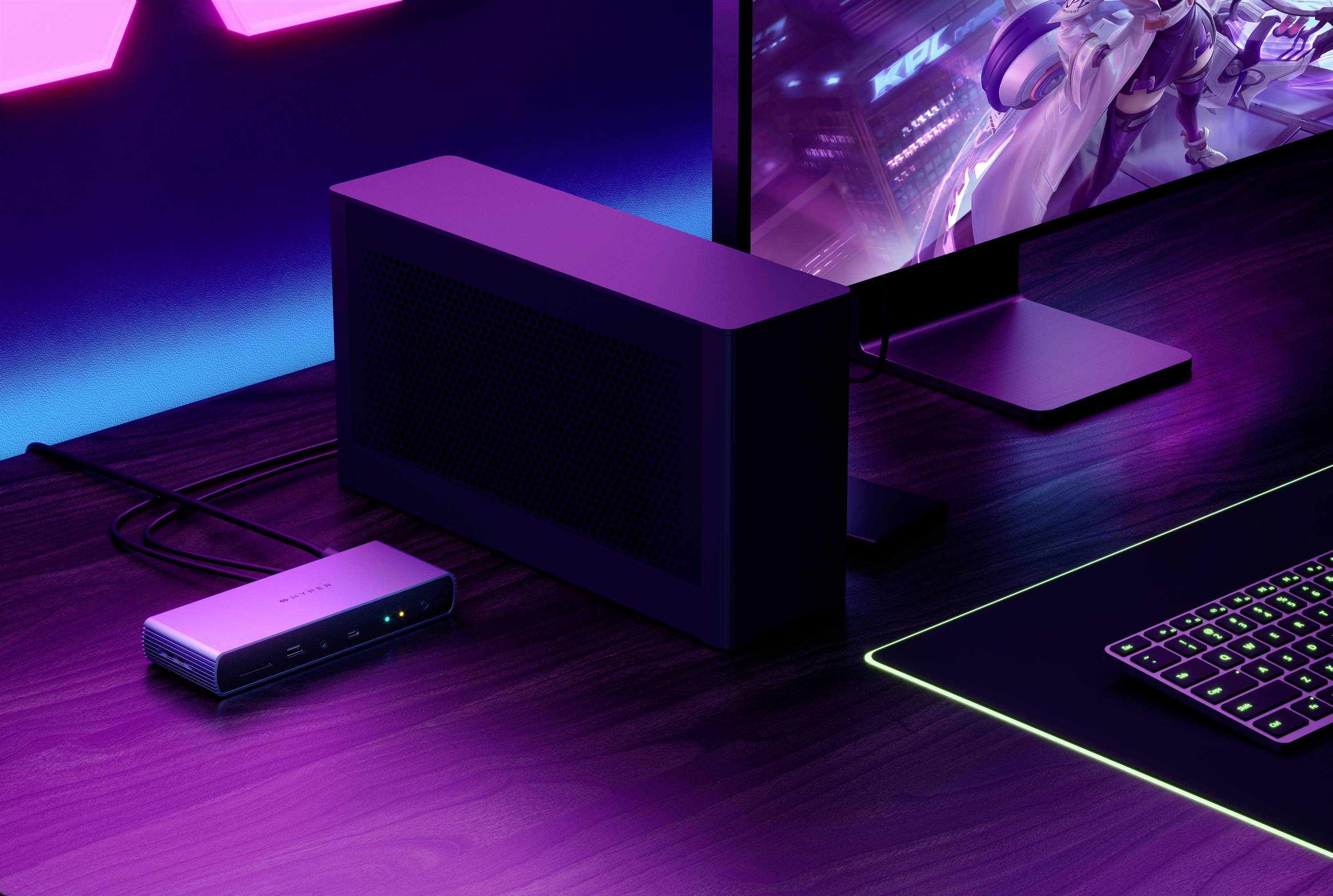 Un posto di lavoro con computer, dotato di tastiera con illuminazione RGB, un monitor moderno e un dispositivo collegato tramite cavi.
