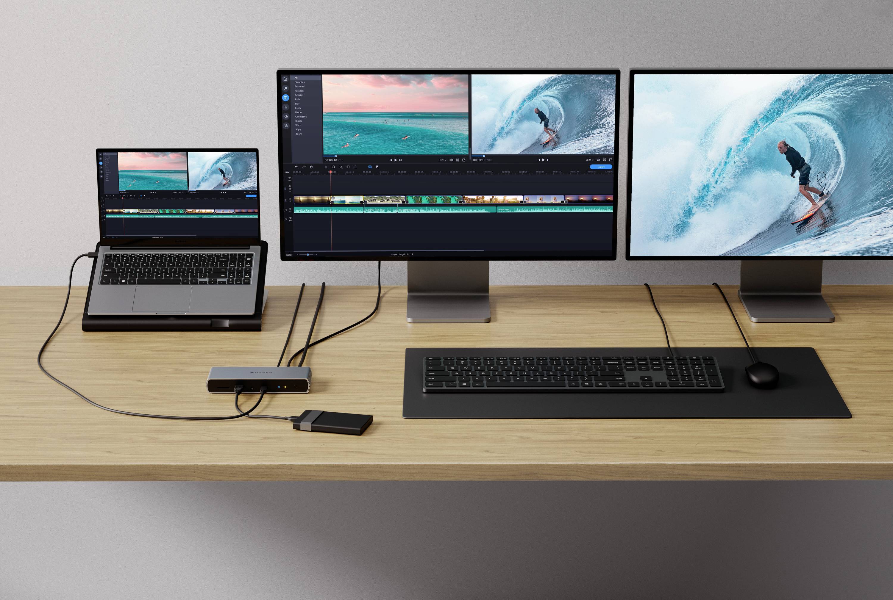 Postazione di lavoro con laptop, due grandi monitor, tastiera e mouse. Sugli schermi è aperto un programma di editing video.