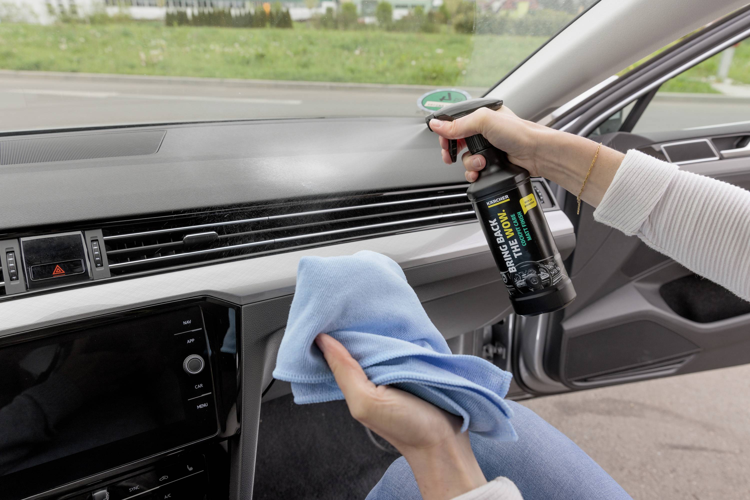 Una persona pulisce l'interno dell'auto con una bottiglia spray e un panno. L'attenzione è concentrata sulla pulizia della plancia.