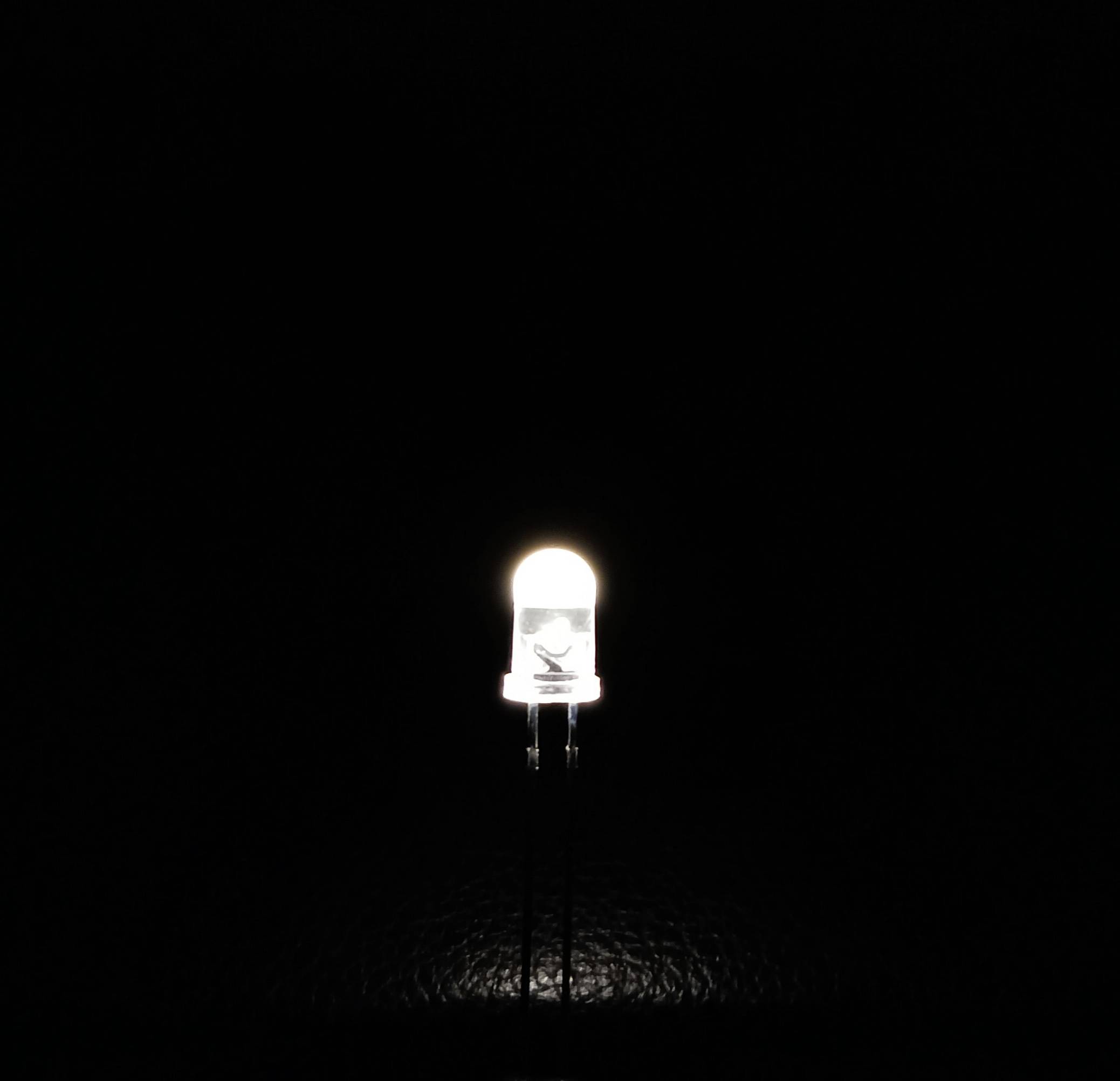 'Primo piano di un singolo LED acceso che emette luce bianca su uno sfondo scuro.'
