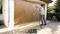 Una persona sta spruzzando vernice per legno su un grande portone del garage utilizzando un sistema a spruzzo. Sullo sfondo sono visibili una casa e un giardino.