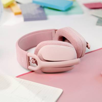 Un paio di cuffie rosa è posizionato su una scrivania bianca, circondato da fogli e blocchi per appunti.