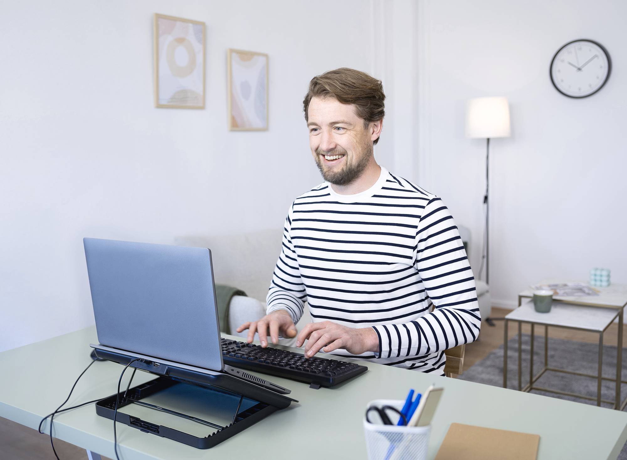 Un uomo con un maglione a righe seduto a un tavolo, che digita su una tastiera davanti a un laptop, sorridendo in un ufficio.