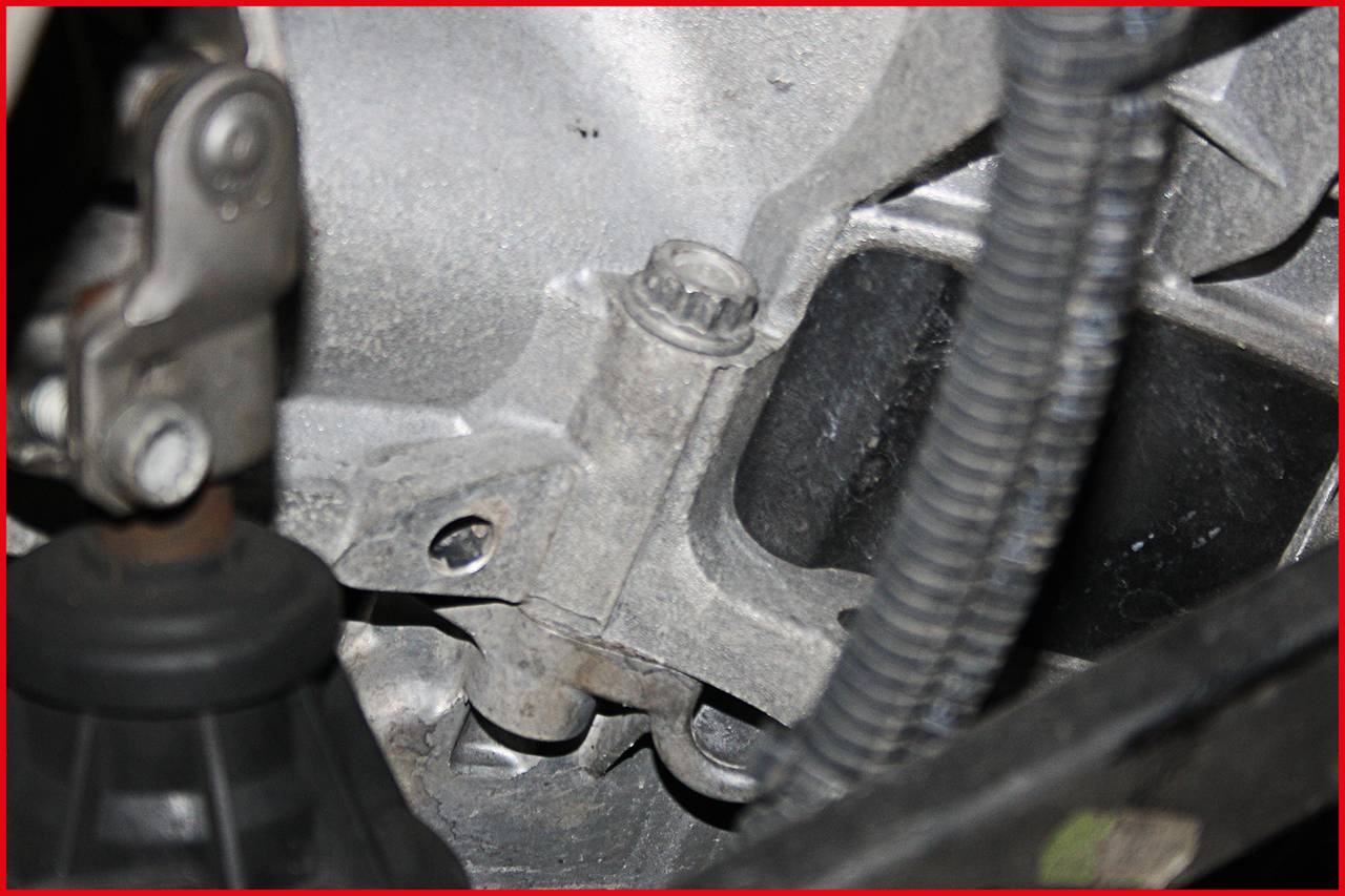 Primo piano di un componente automobilistico nel vano motore con connessioni metalliche e cavi. Attenzione principale sul componente meccanico.